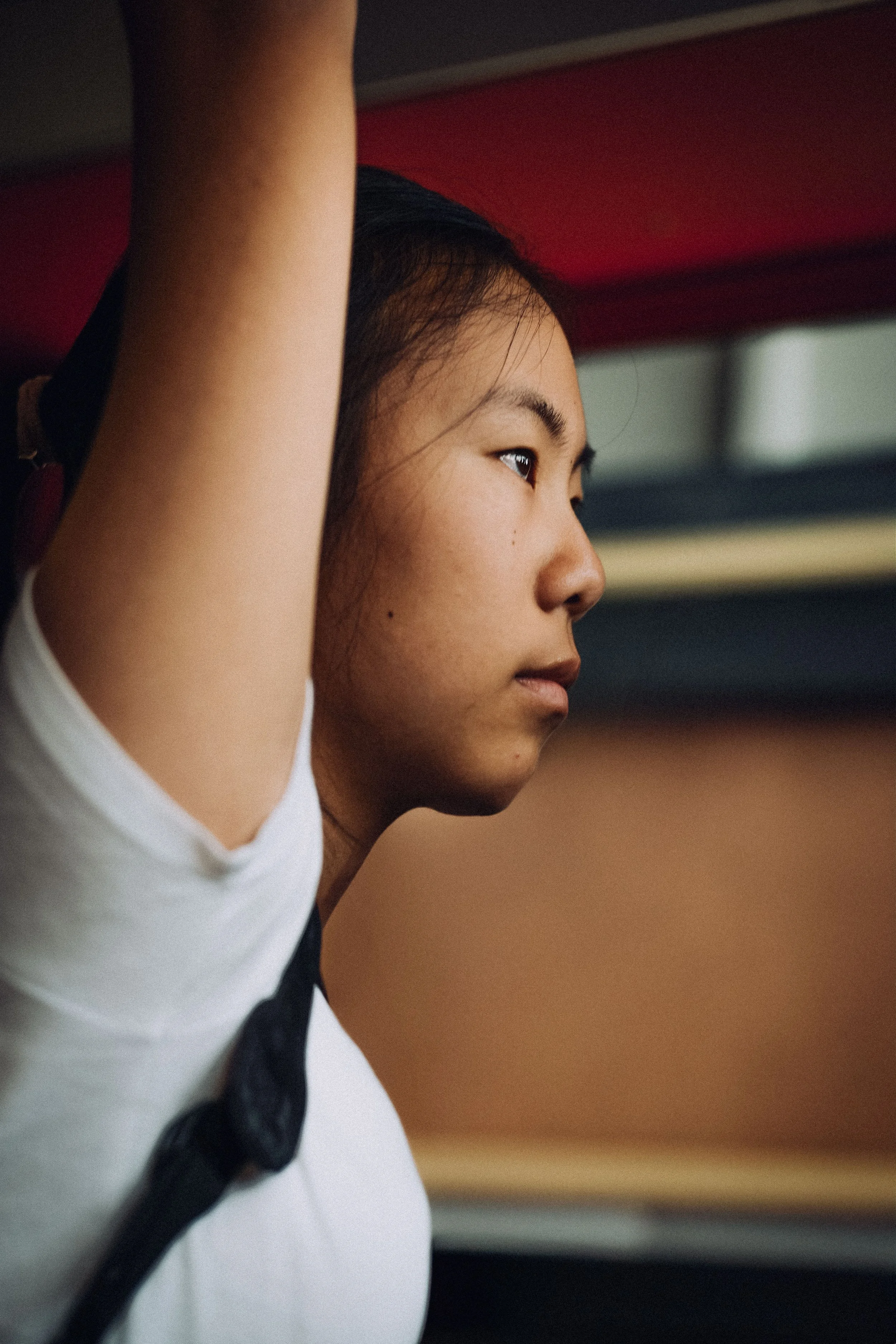 A young woman with dark hair pulled back, wearing a white shirt, resting her arm on a surface and looking focused.