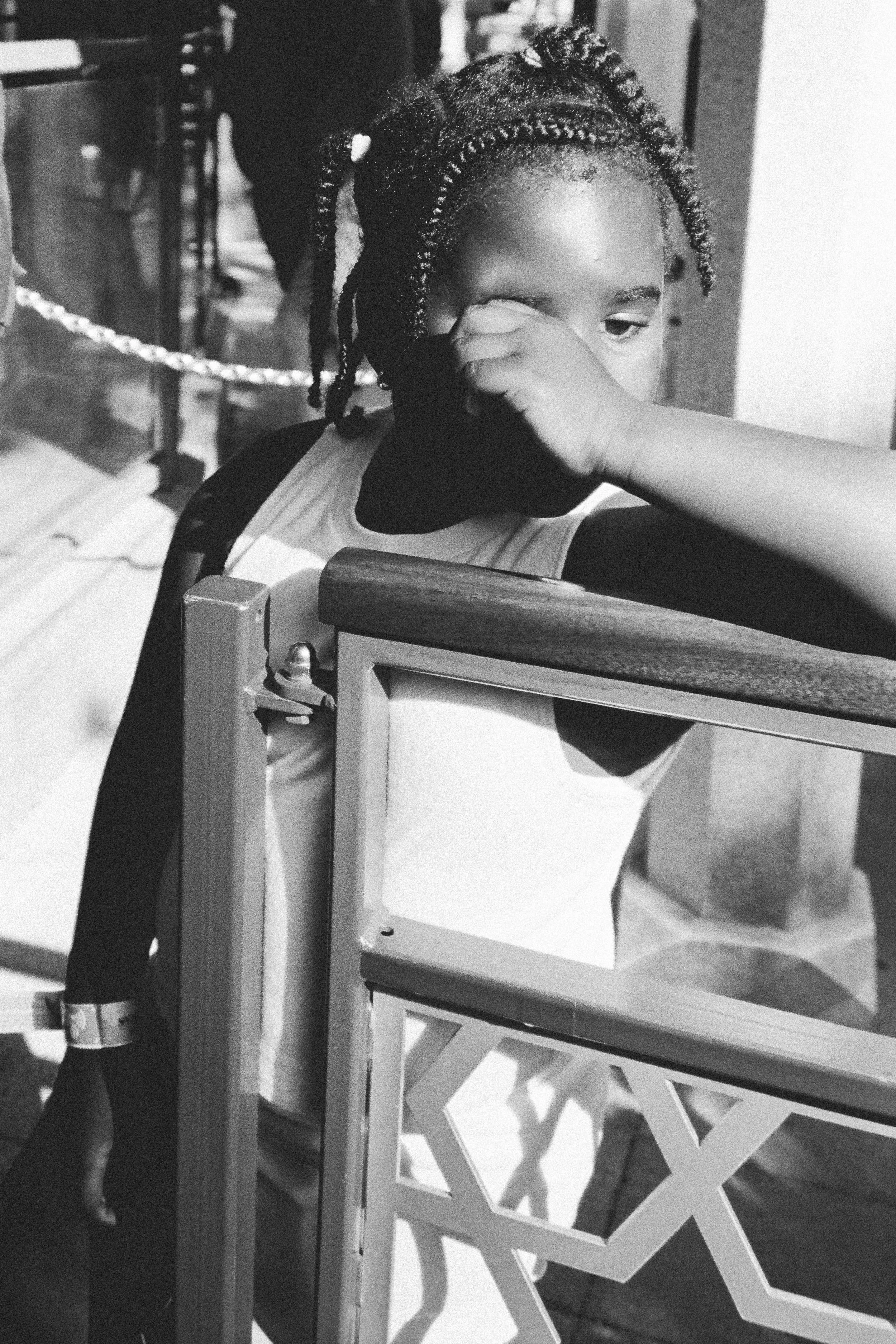 A young girl with braided hair wiping her eyes with her hand, leaning on a wooden railing.