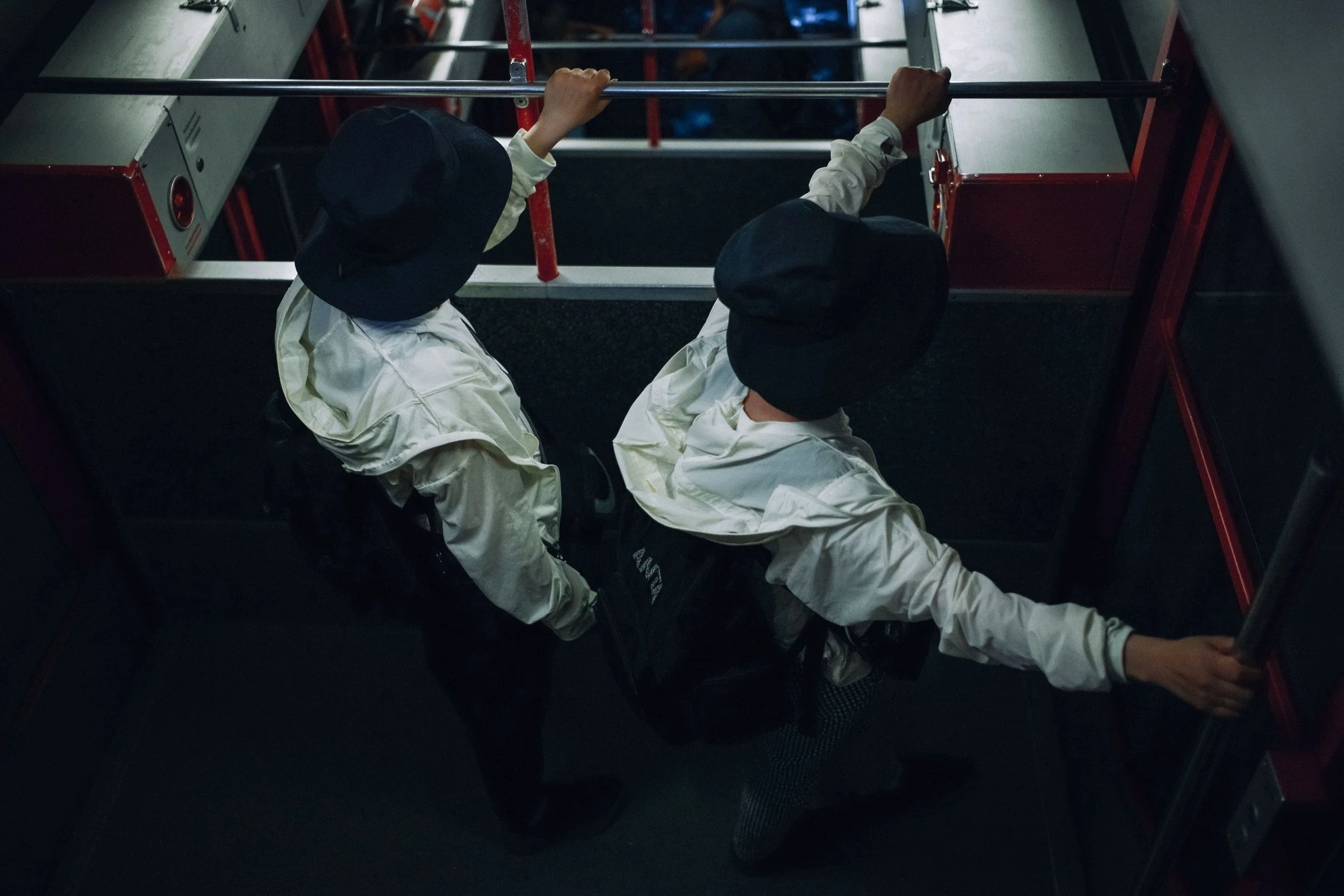 Two firefighters in white jackets and black helmets are climbing an escalator, holding onto the handrails.