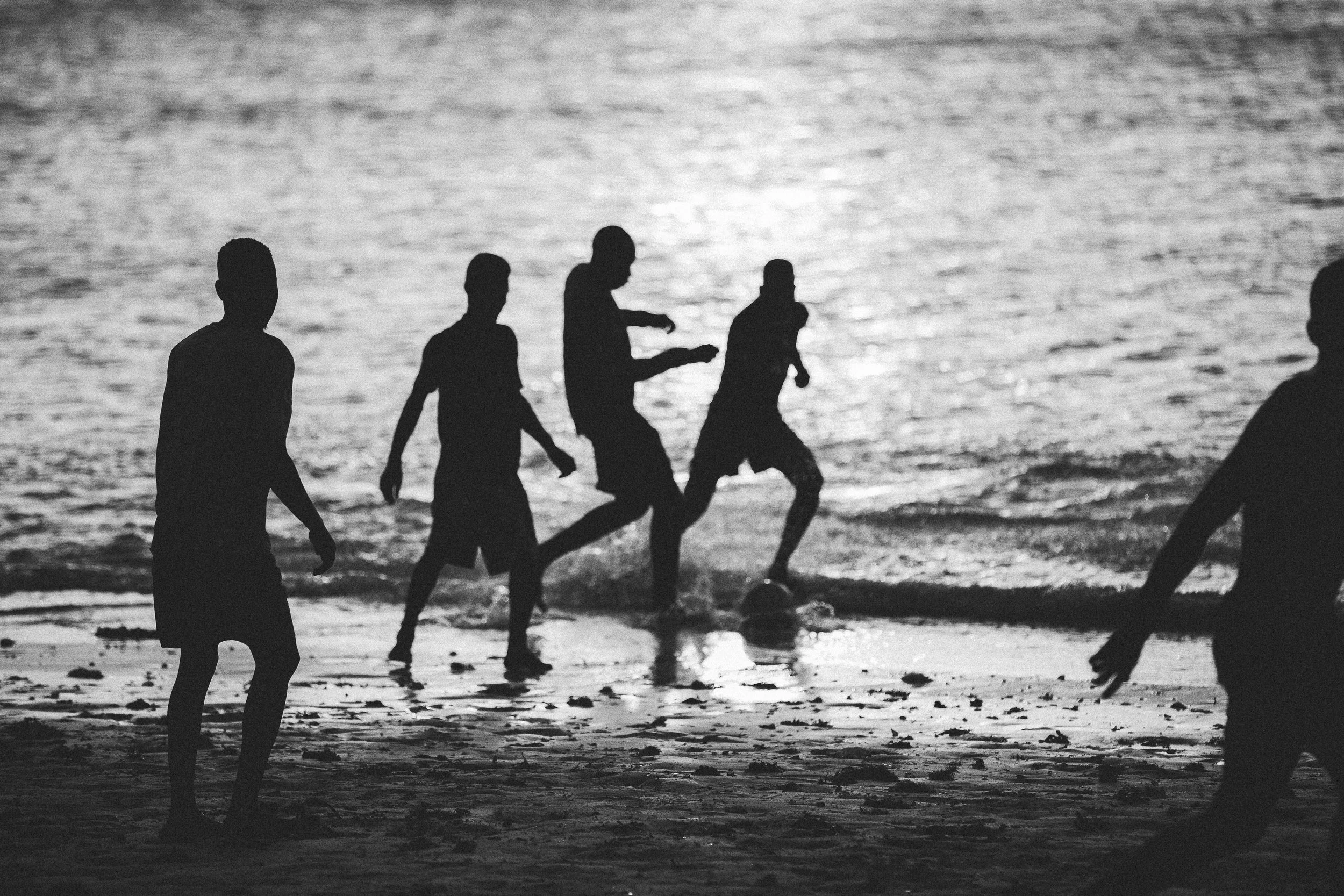 Silhouettes of children playing soccer on the beach at sunset or sunrise