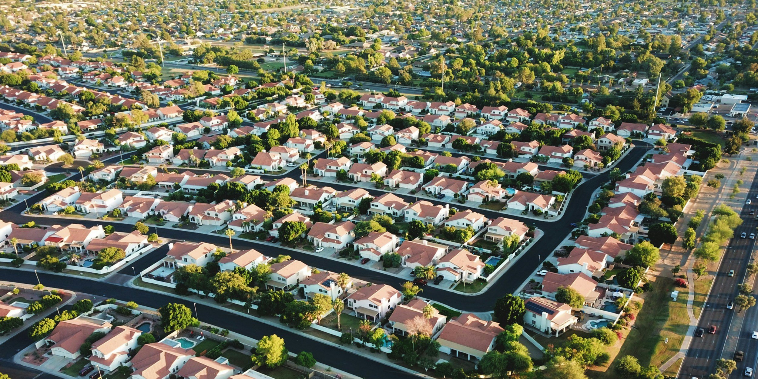Aerial view of a suburban neighborhood with rows of houses, green lawns, and roads.