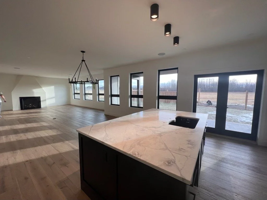 Empty open-concept living room and kitchen with hardwood floors, large windows, a fireplace, a chandelier, and sliding glass doors leading to an outdoor area.