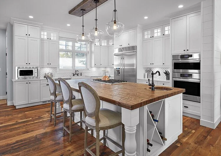 Modern white kitchen with wooden island, pendant lights, and stainless steel appliances.