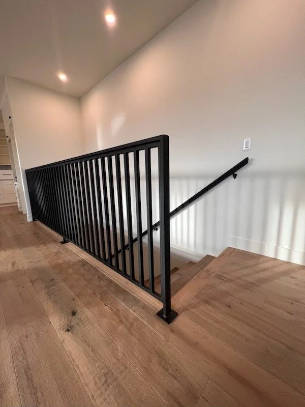 Interior staircase with a black metal railing and wooden flooring, leading downward to another floor.