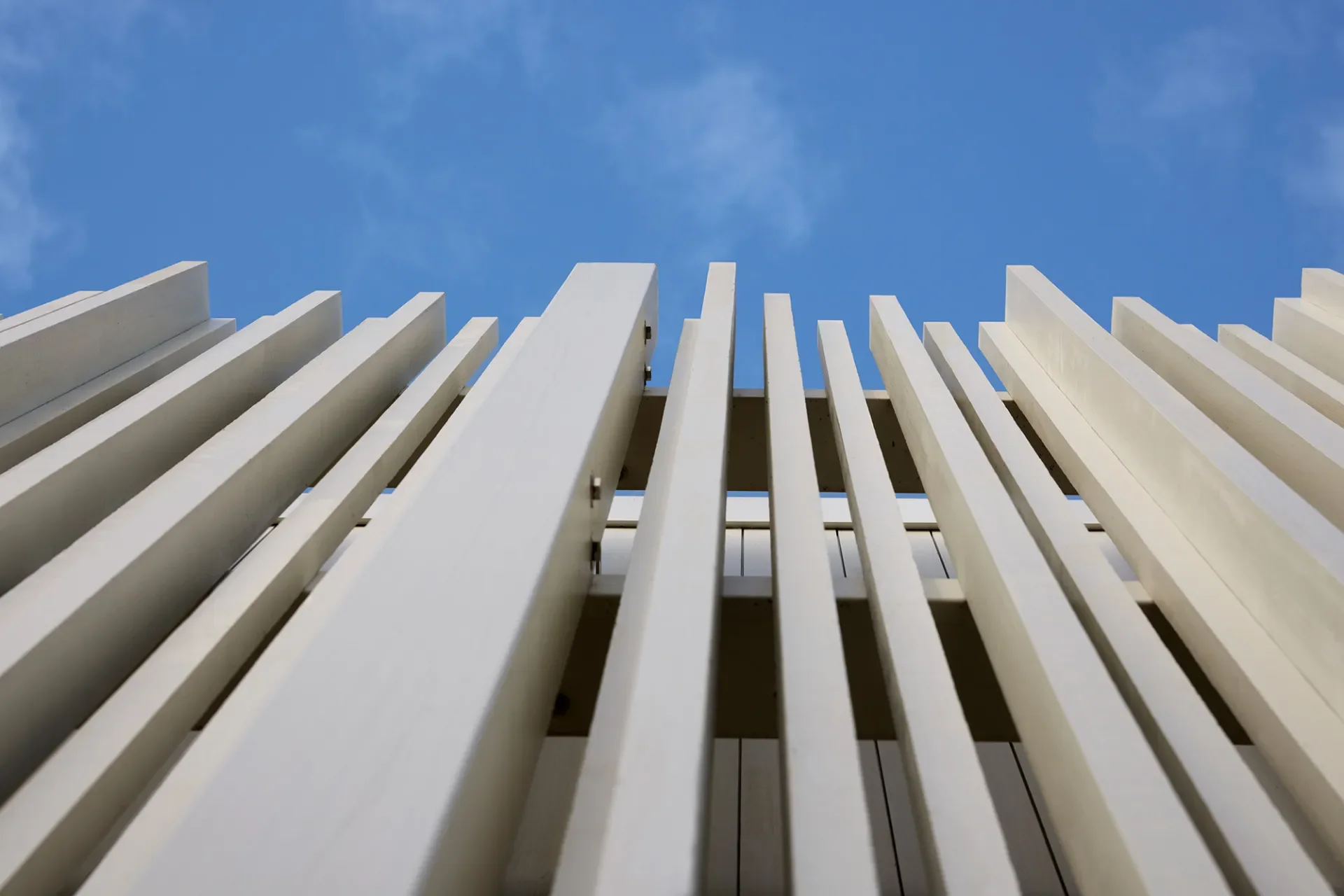 White wooden slats arranged vertically on a structure against a blue sky with few clouds.