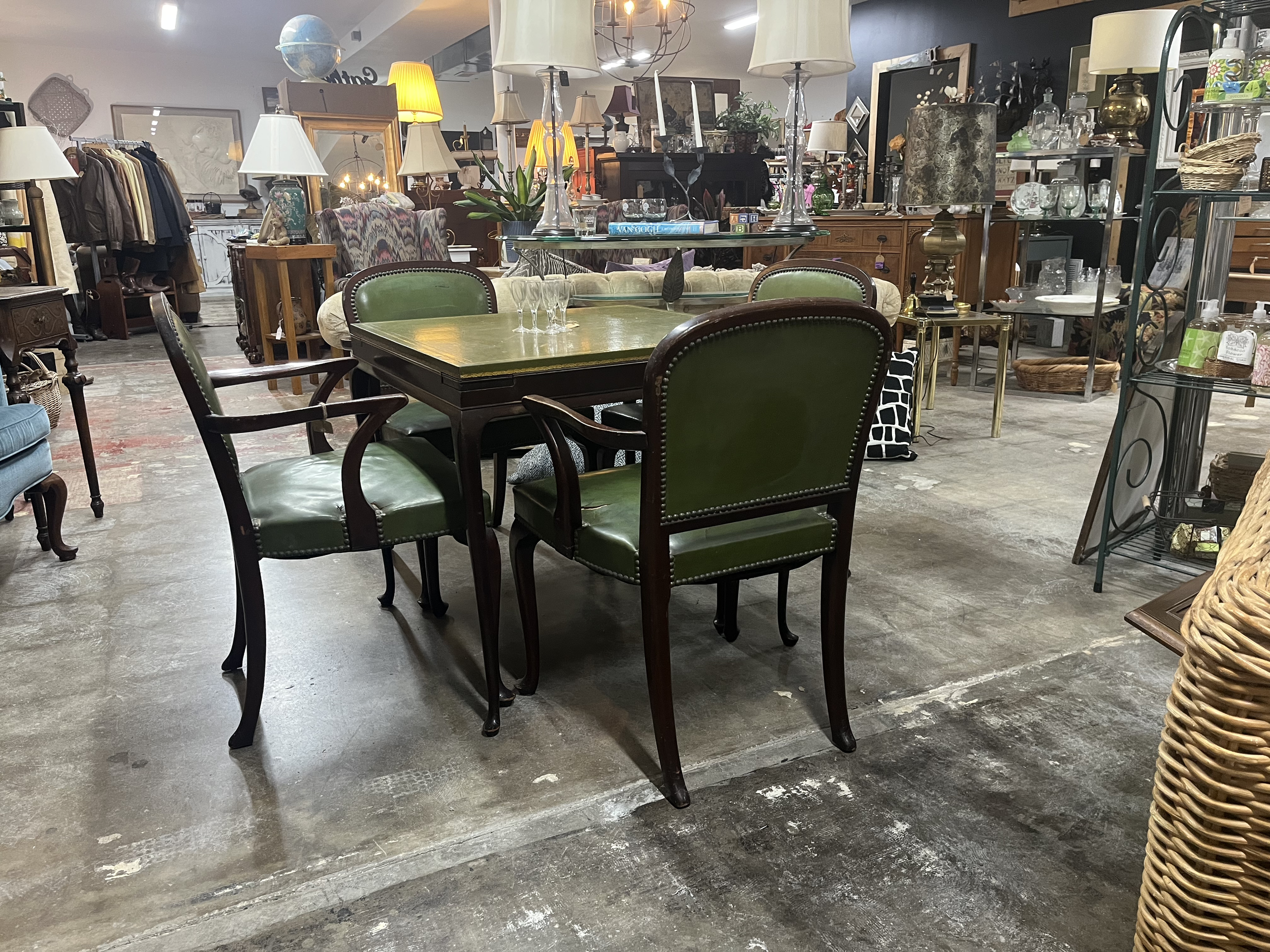 A furniture store displaying various vintage and antique furniture pieces, including a table with four green leather armchairs, lamps, and decorative items on shelves and tables.