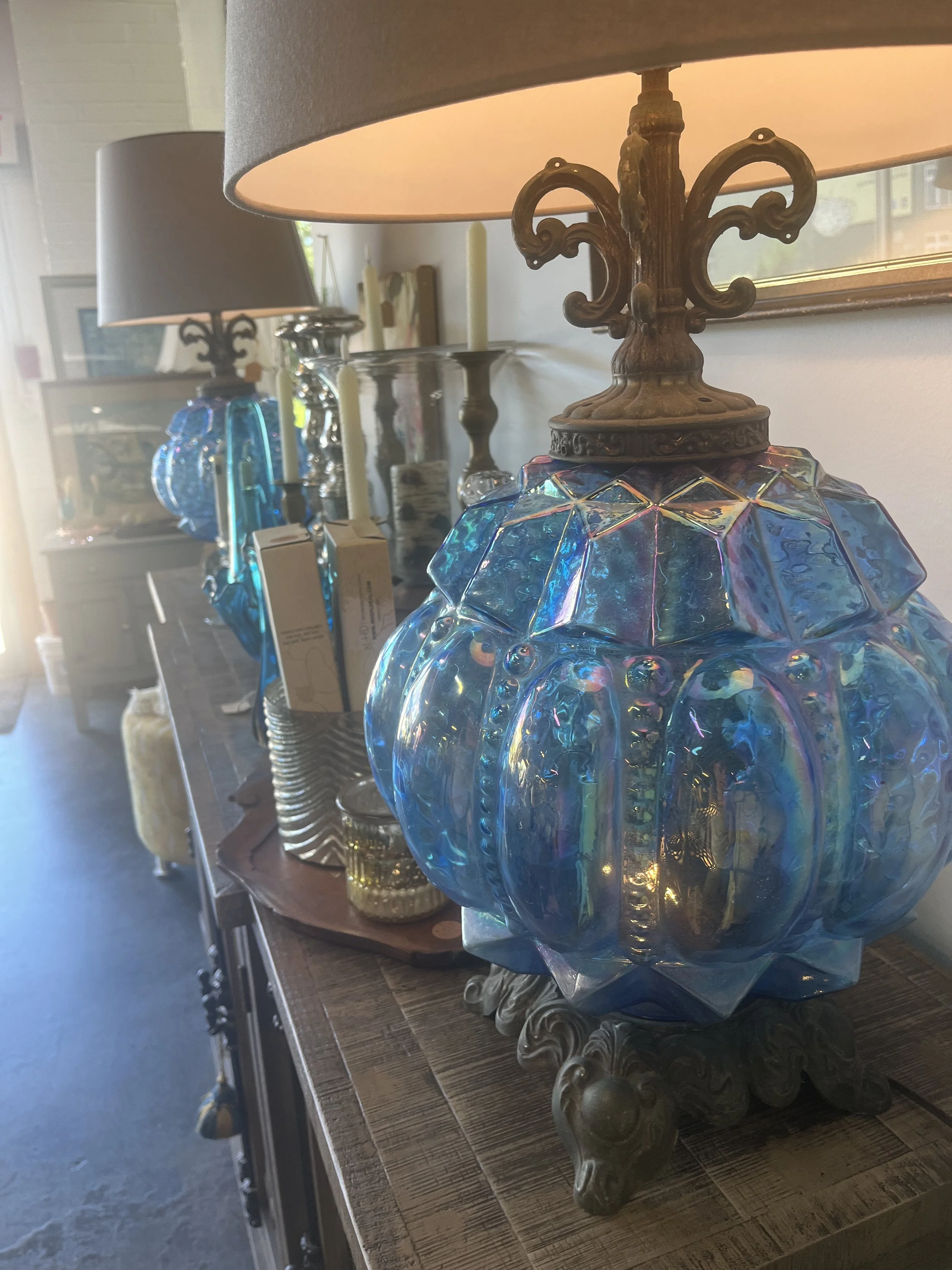 Decorative iridescent glass lamp with ornate bronze base and lampshade on wooden sideboard.