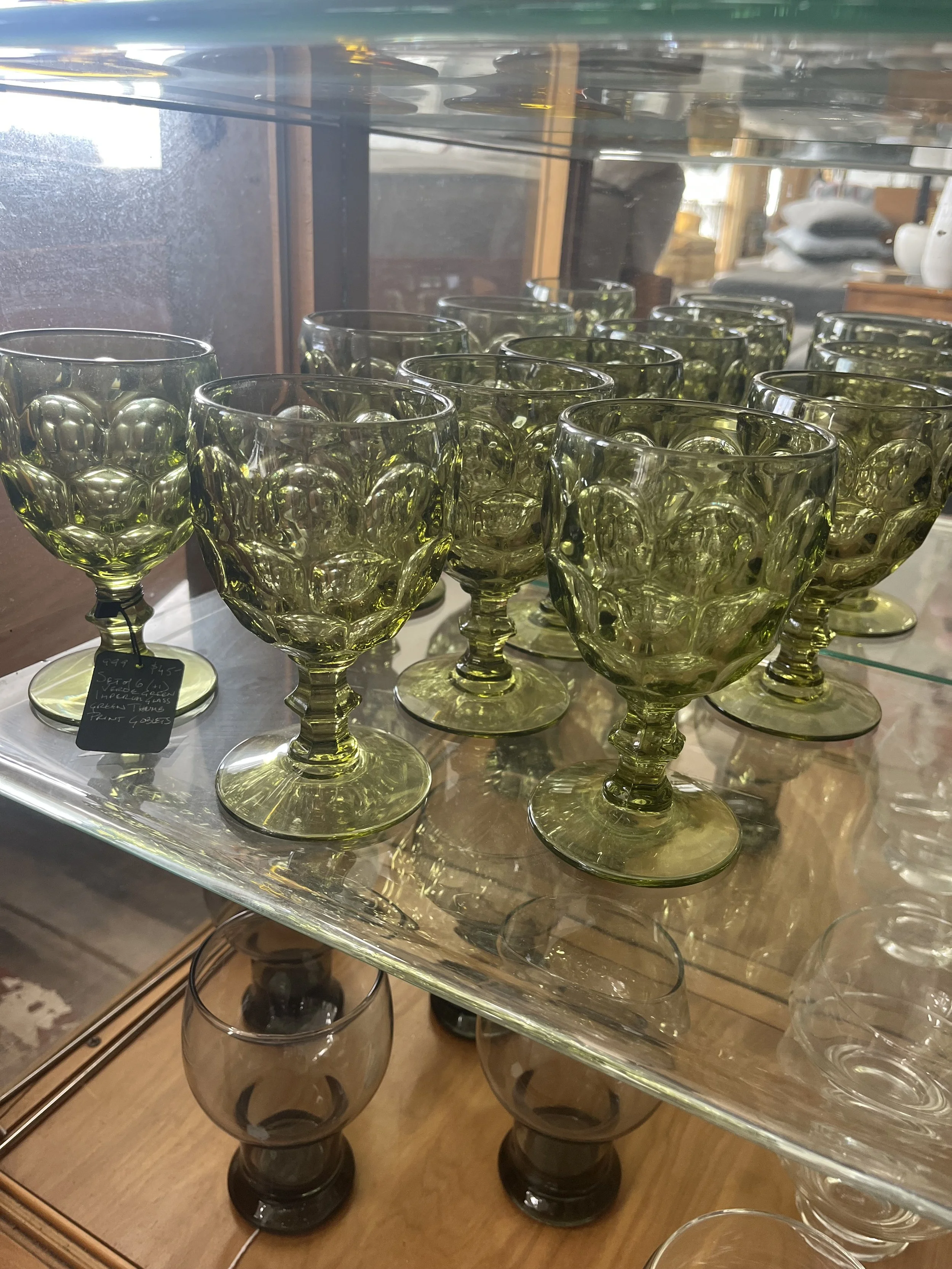 Set of green glass goblets with bubble pattern on a display shelf in a store.