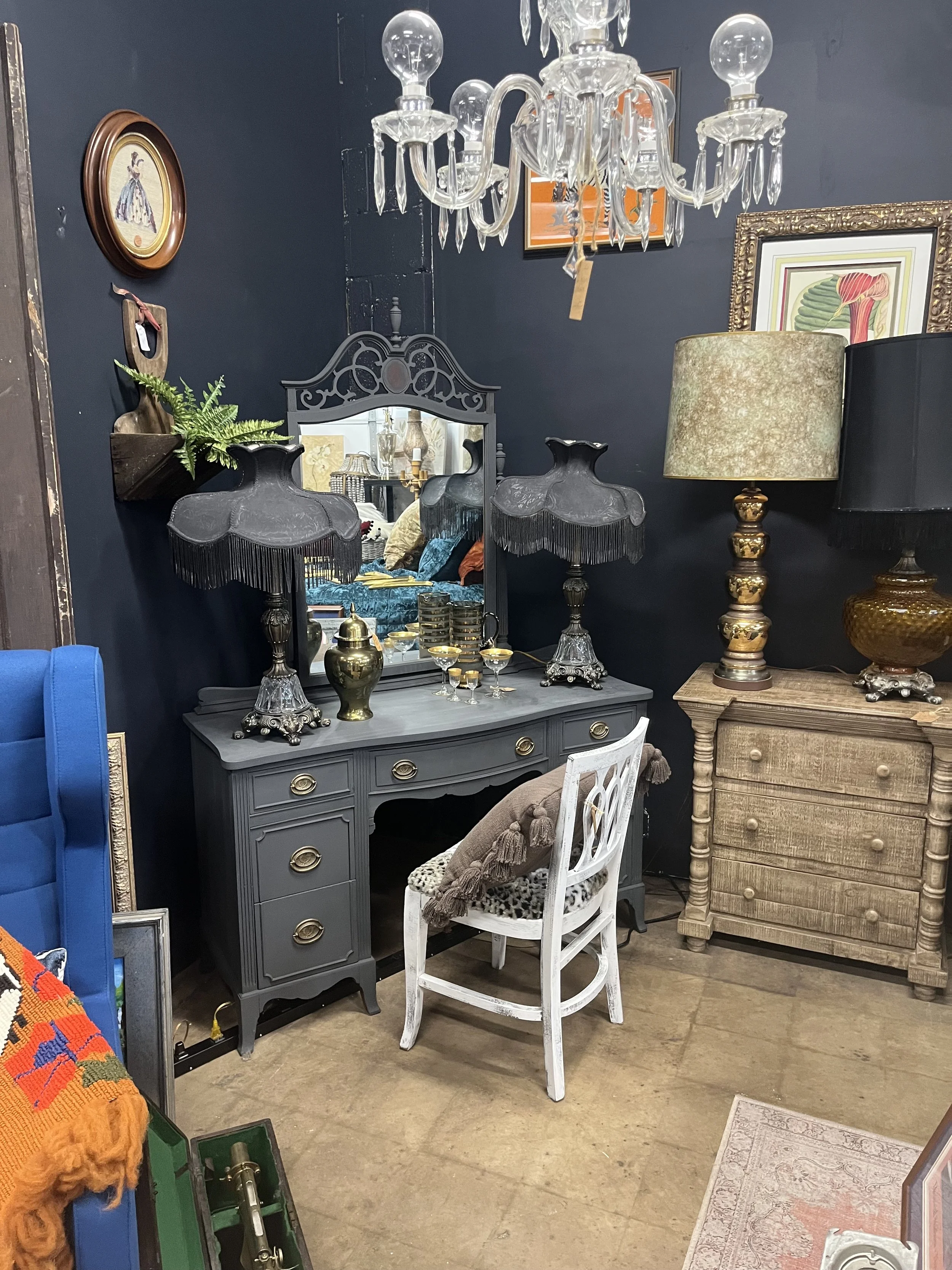 An antique-style dresser with a mirror, black lamps with fringed shades, and decorative items on top, set against a dark wall in a vintage home decor room.