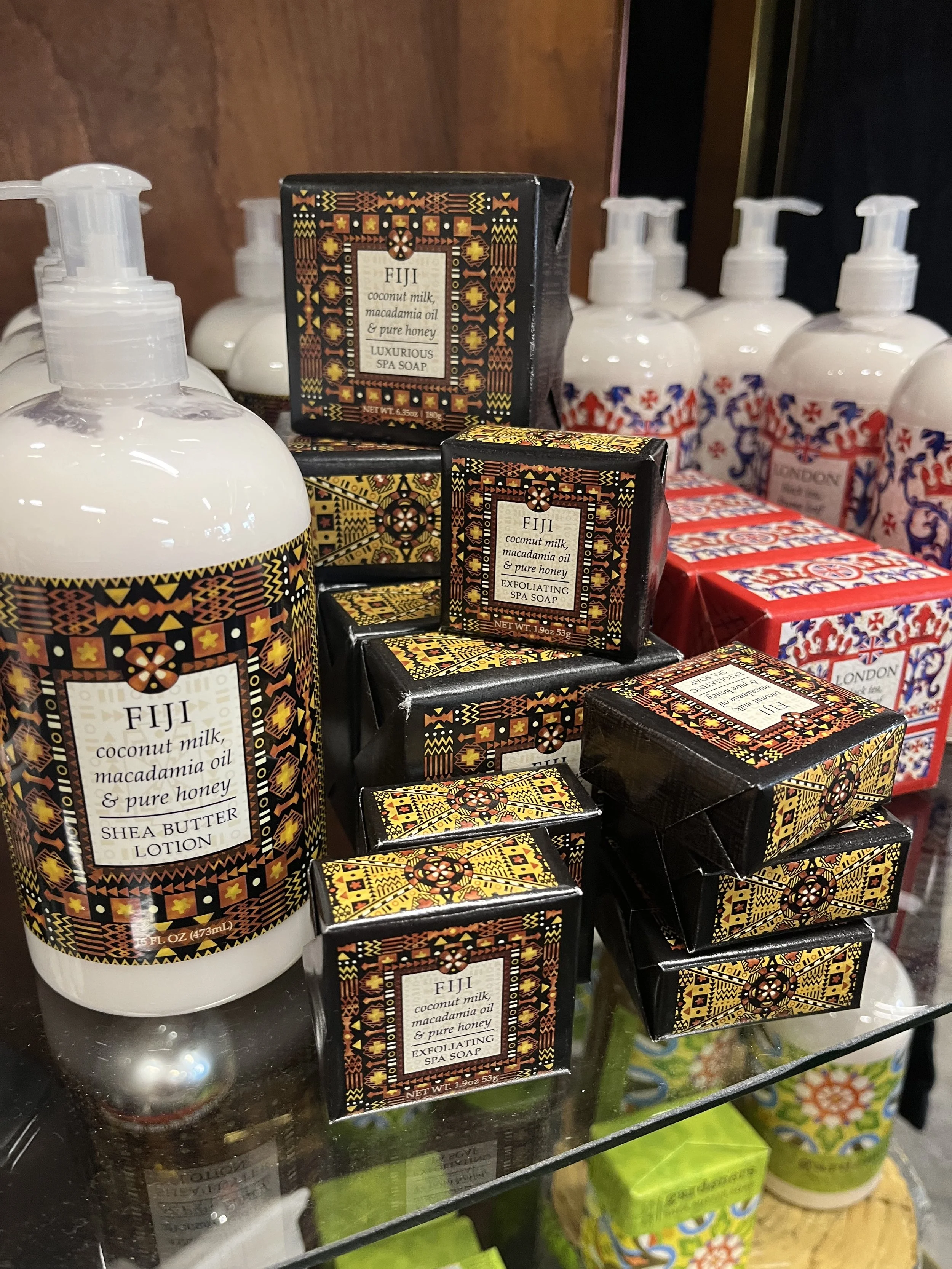Display of Fiji spa products including coconut milk, macadamia oil, pure honey, shea butter lotion, and exfoliating spa soap on a glass shelf.