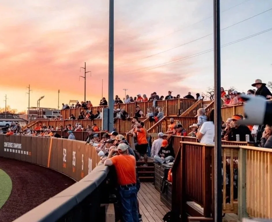 Baseball stadium with spectators seated on wooden bleachers during sunset.