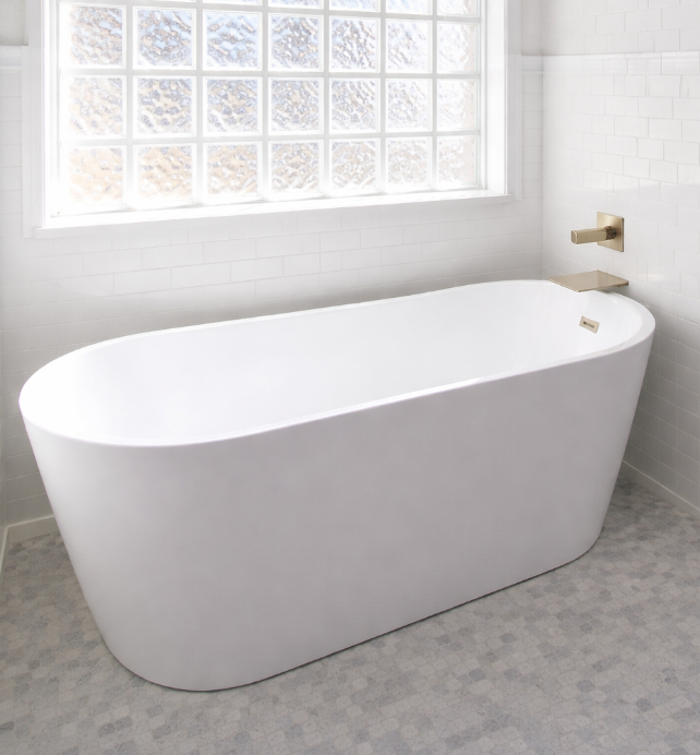 White freestanding bathtub in a modern bathroom with white tiles and glass block window