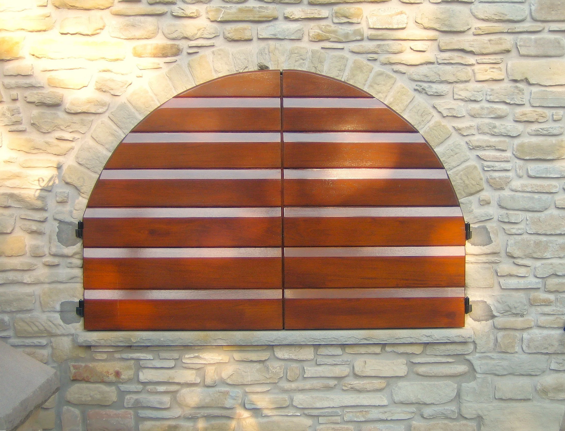 Una finestra con persiane di legno chiuse, con archi a forma di semicerchio, installata su un muro di pietra chiara
