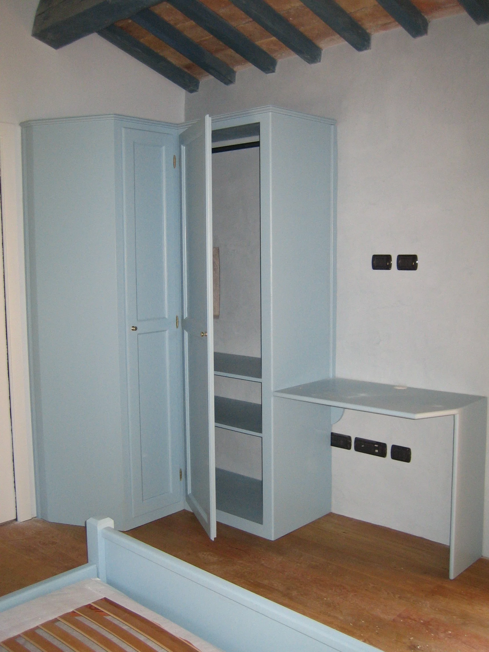 Mobili e armadi color celeste in una stanza con soffitto a travi in legno.