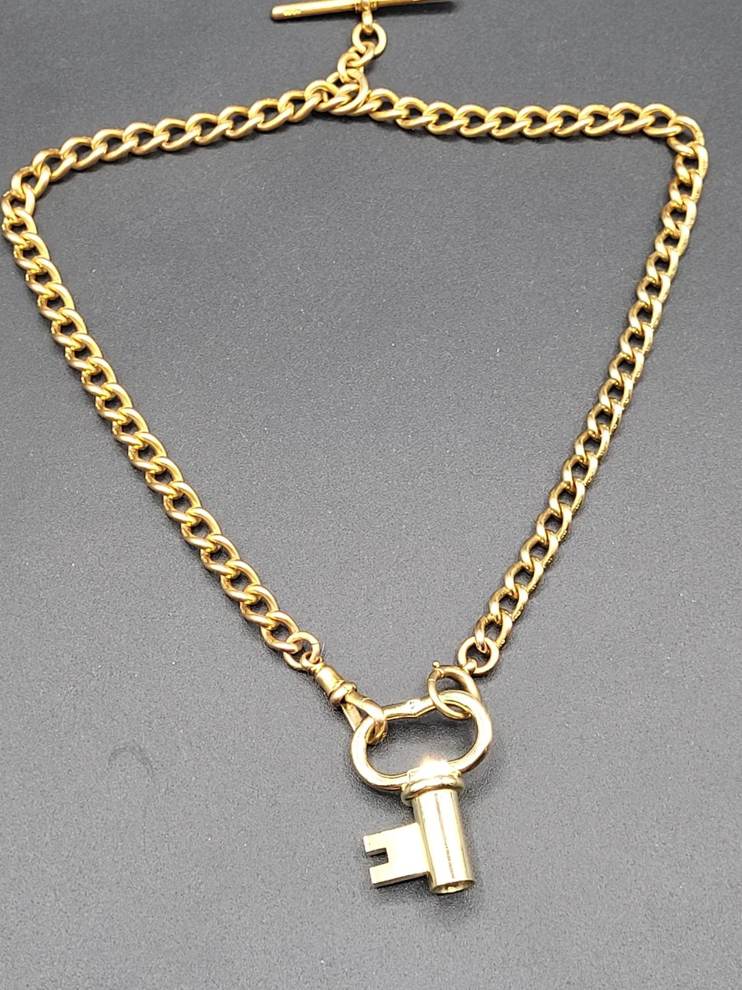 Gold chain necklace with a lock and key pendant on a black background.