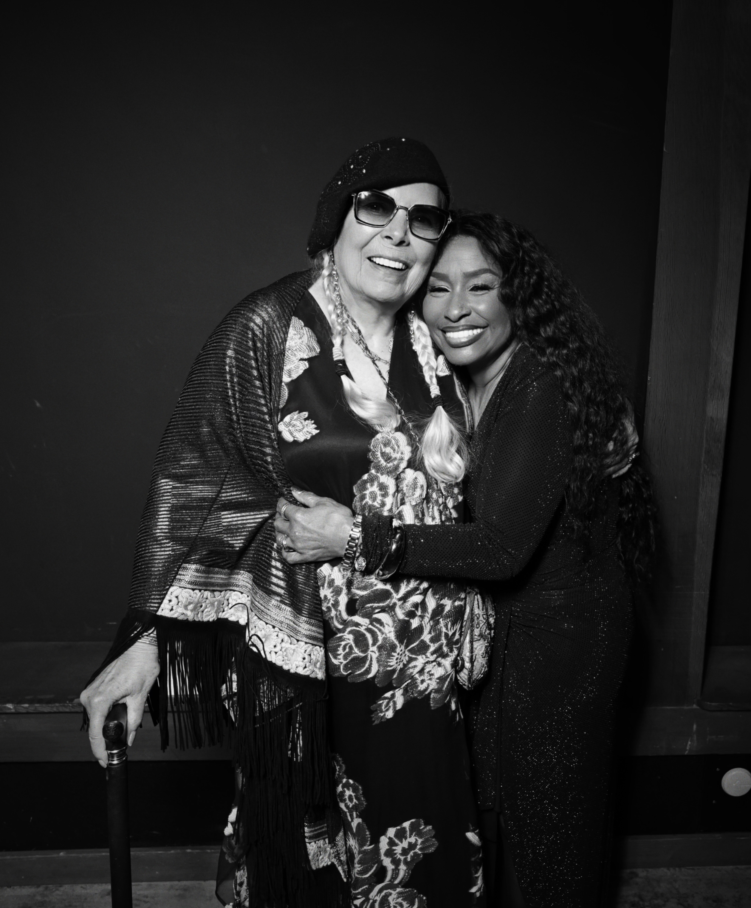 Two women hugging, smiling, and facing the camera in a black and white photo.
