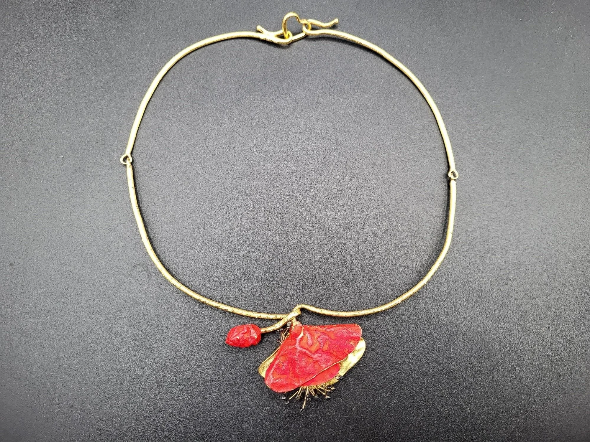 Gold necklace with a red and gold butterfly pendant and a small red bead charm placed on a dark surface.