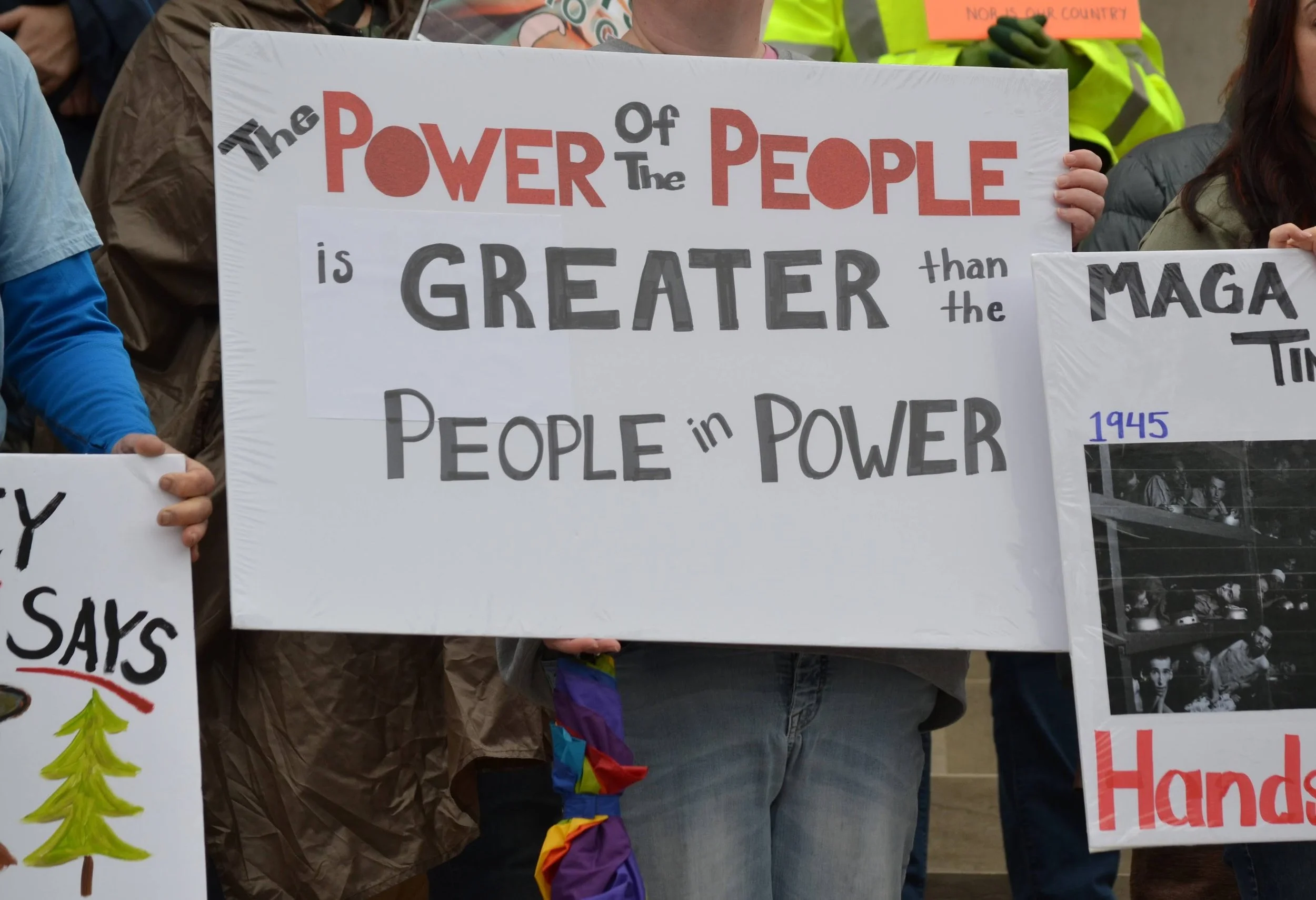 Protest sign reading 'The power of the people is greater than the people in power' held by protestors.