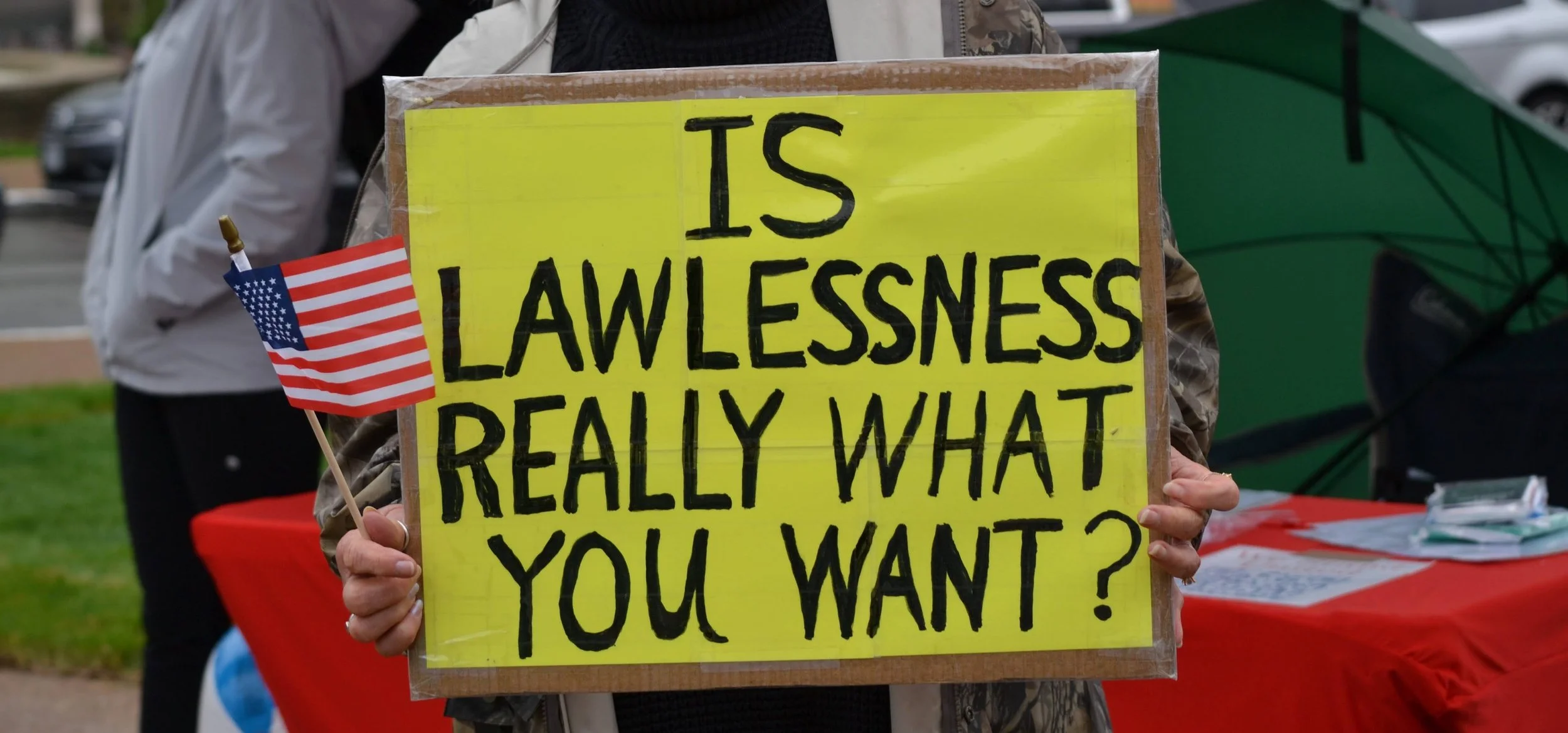 A protester holding a yellow sign that reads, 'Is Lawlessness Really What You Want?' with a small American flag attached.