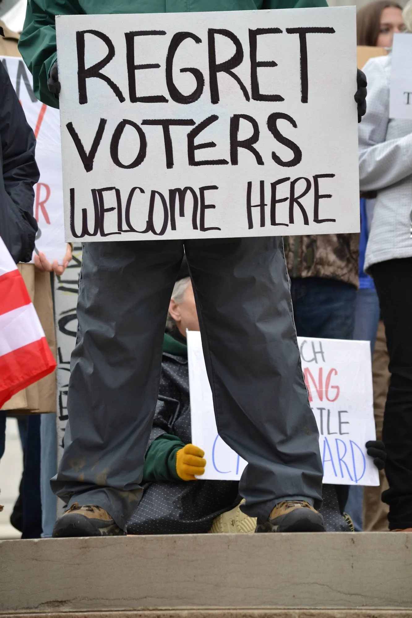 Protestor holding a sign reading 'Regret Voters Welcome Here' at a rally.