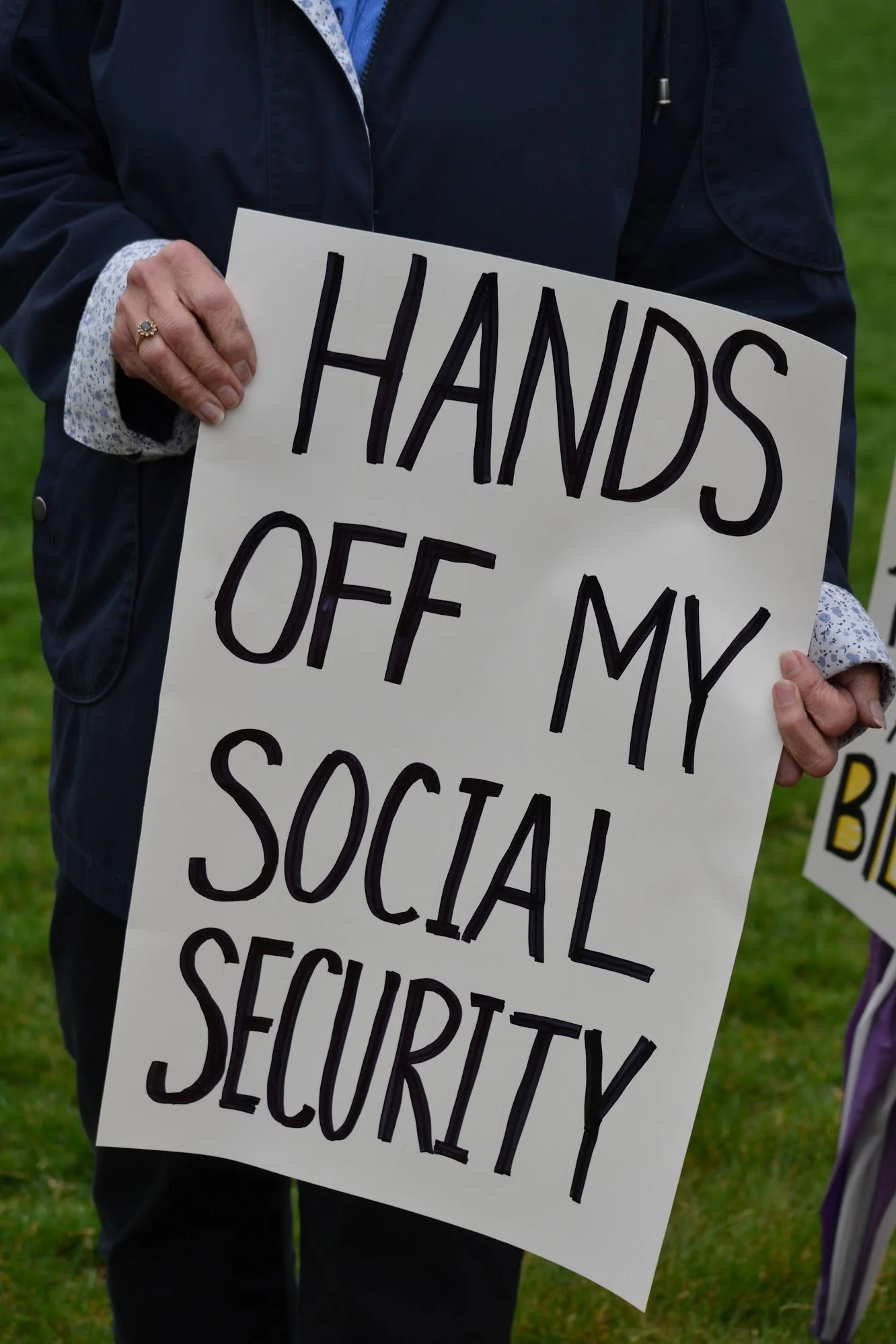 Person holding a sign that says 'Hands Off My Social Security'.