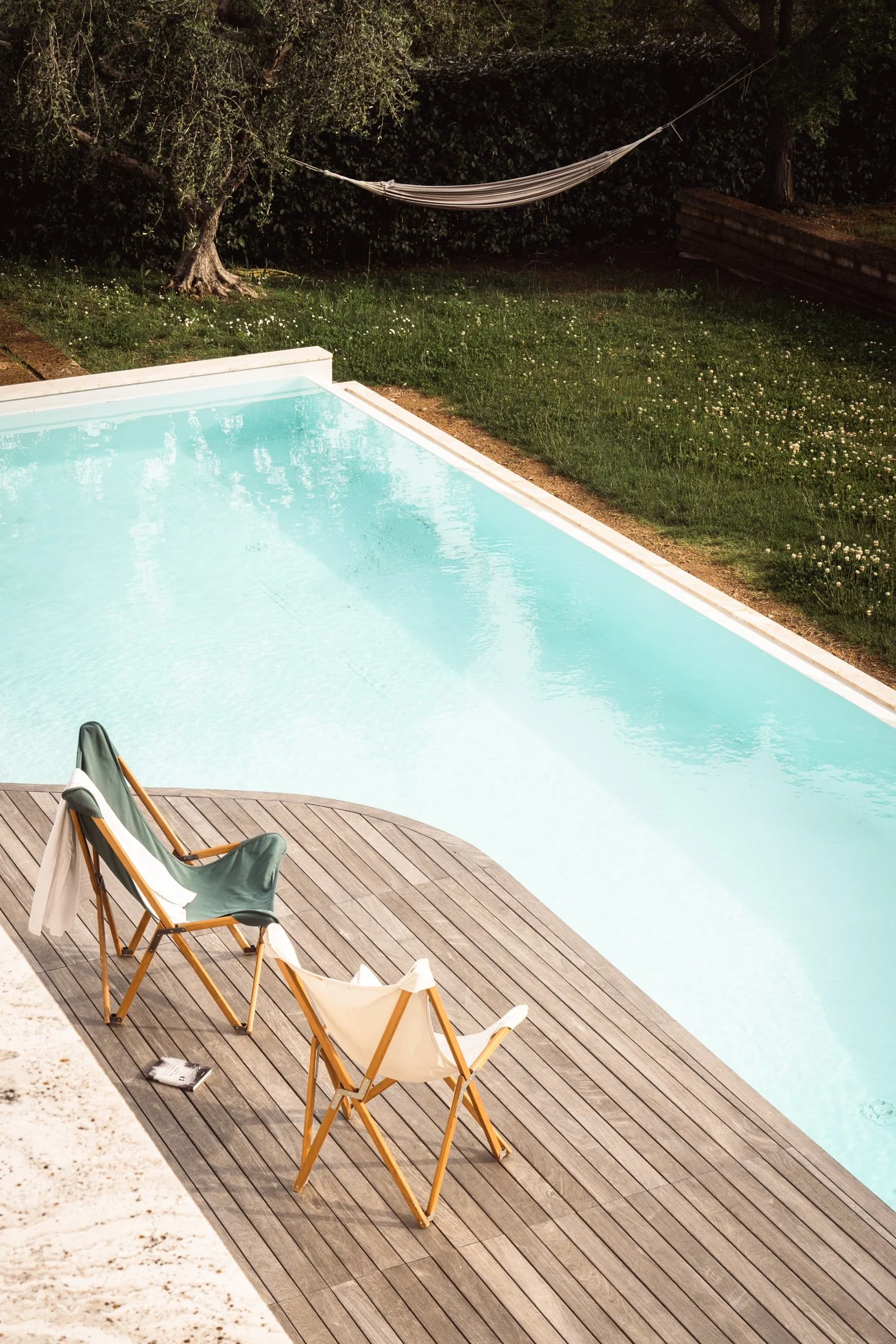 Modern beach chairs by a beautiful turquoise pool set in the middle of an Italian olive grove in Tuscany
