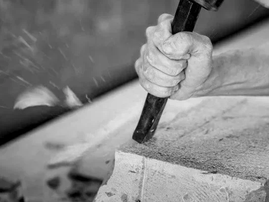 A person holding a chisel and working on a large block of stone.