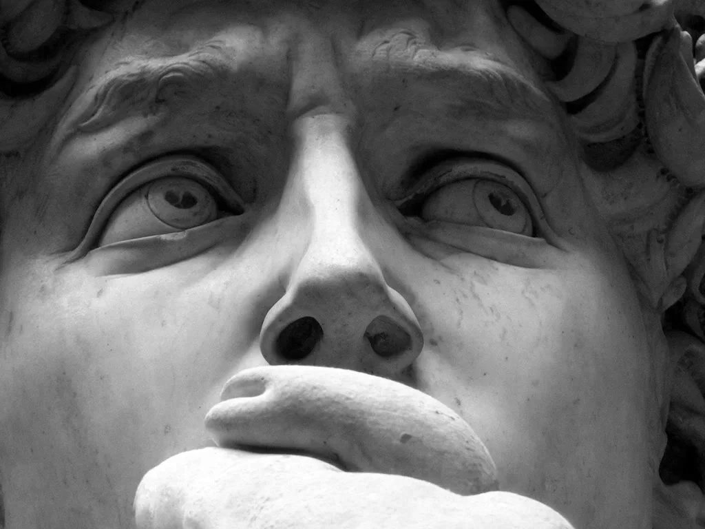 Close-up of the sculpture of a person's face with a hand covering their mouth, focusing on the eyes, nose, and lips.