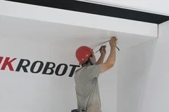 Une personne en train de fixer quelque chose au mur à l'aide d'un outil. On voit un logo partiel qui semble dire 'ROBOT'.