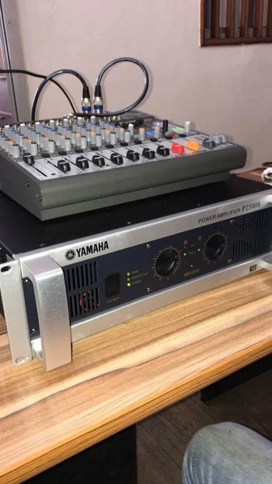 Une table en bois avec un amplificateur Yamaha P2500S en dessous et une table de mixage audio au-dessus.