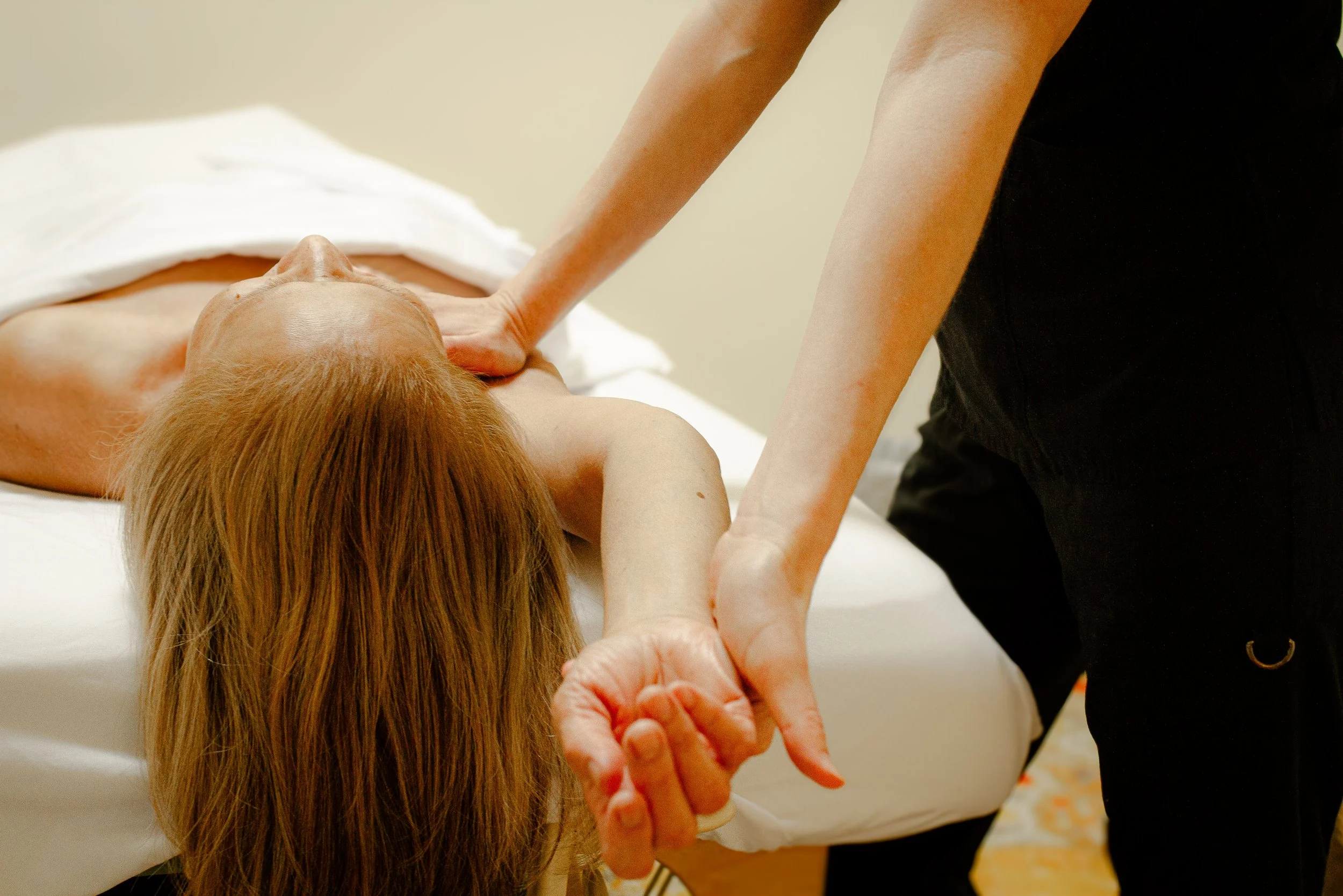 A myofascial release practitioner supports a client's shoulder and outstretched arm during treatment.
