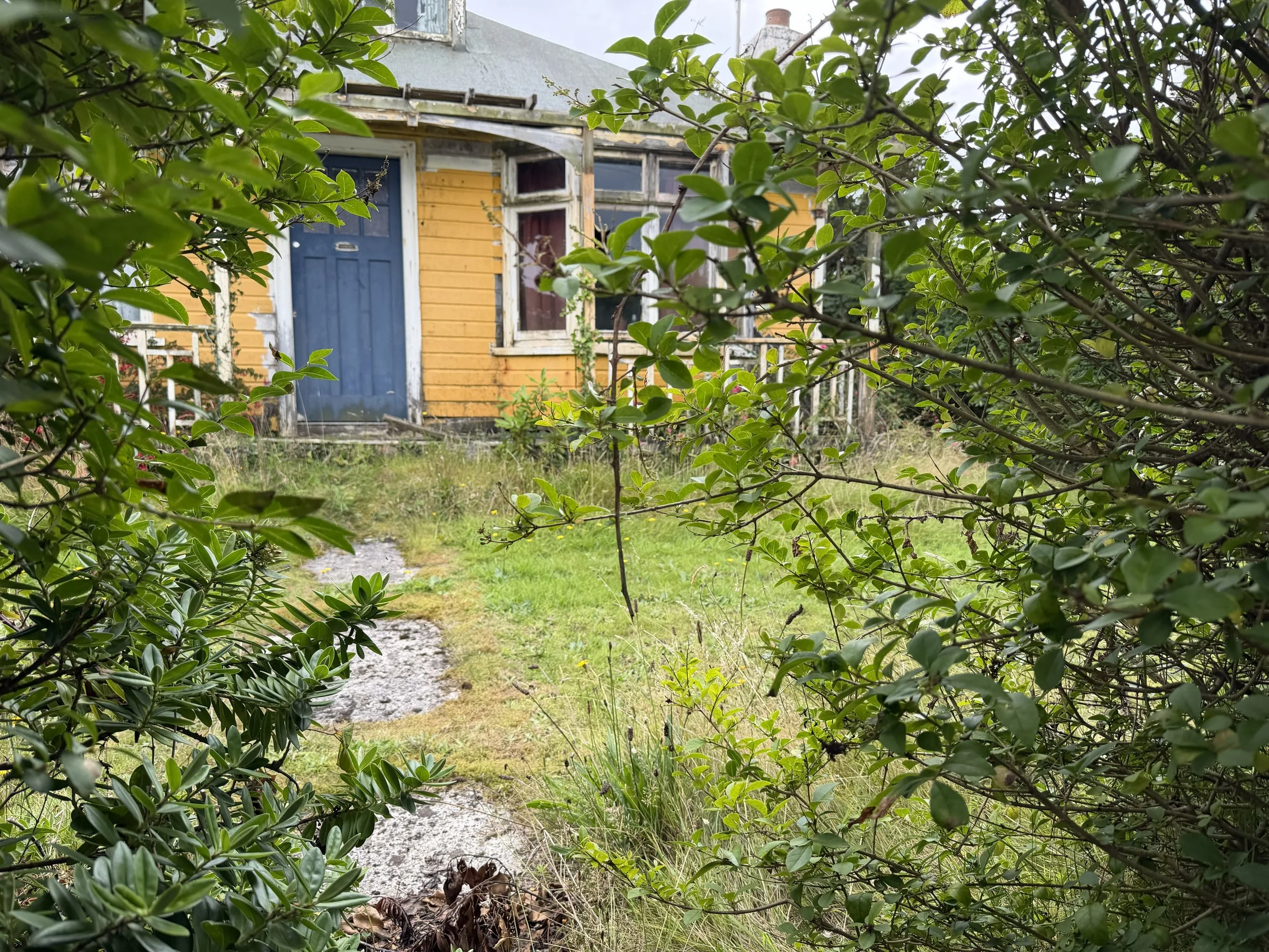 A yellow-painted clapboard chalet with a veranda in a hedged and gated garden