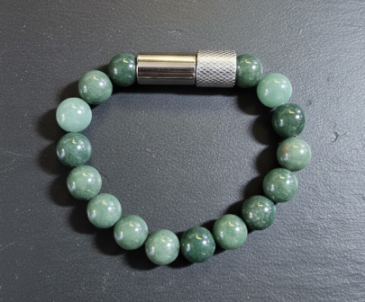 Beaded bracelet with green and white beads and a metallic clasp on a dark surface.
