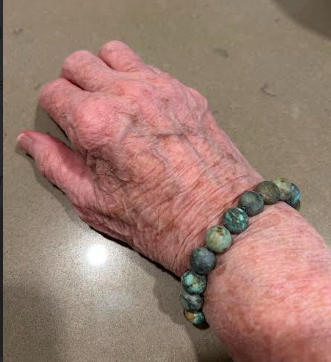 Elderly hand wearing turquoise Enusia pill holder bracelet – Comfortable and discreet pill holder bracelet for seniors, offering peace of mind for daily medication needs.