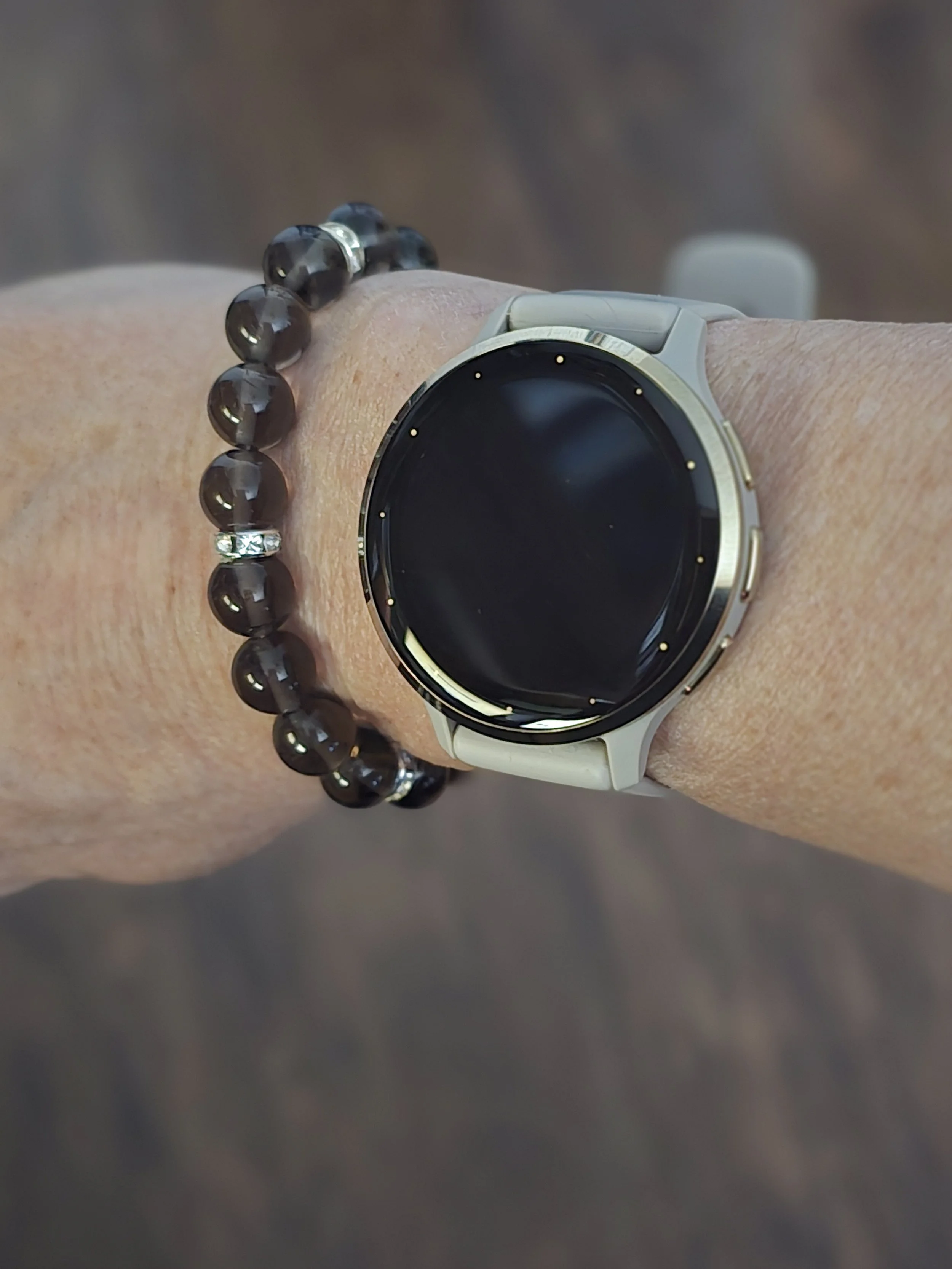 Woman’s wrist with black Enusia pill holder bracelet stacked with a smartwatch – Elegant and functional pill holder bracelet for women, discreetly storing daily or emergency medication.
