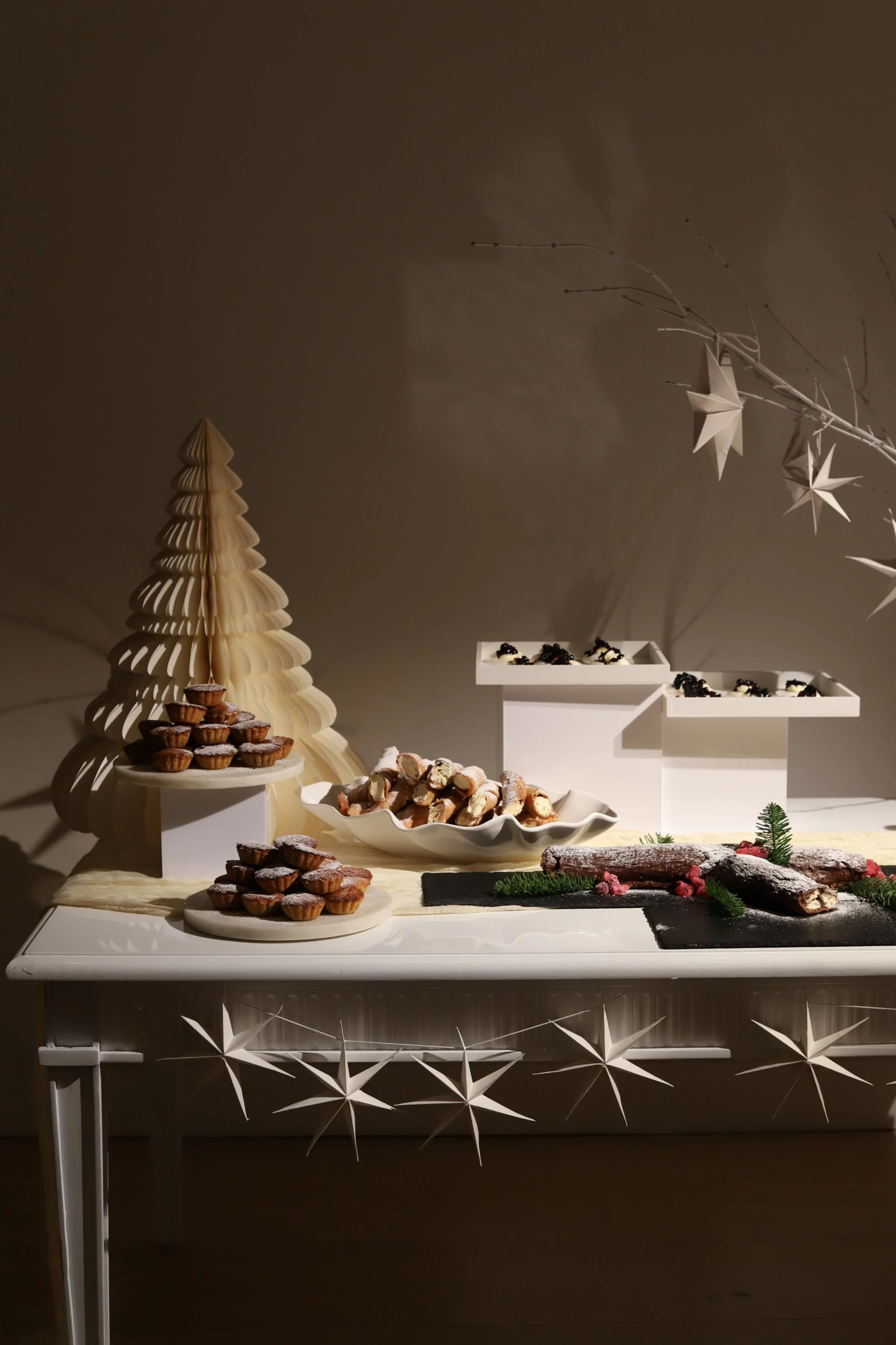 Holiday food dessert table with mince pies, cannoli, and desserts, decorated with Christmas and winter-themed ornaments.
