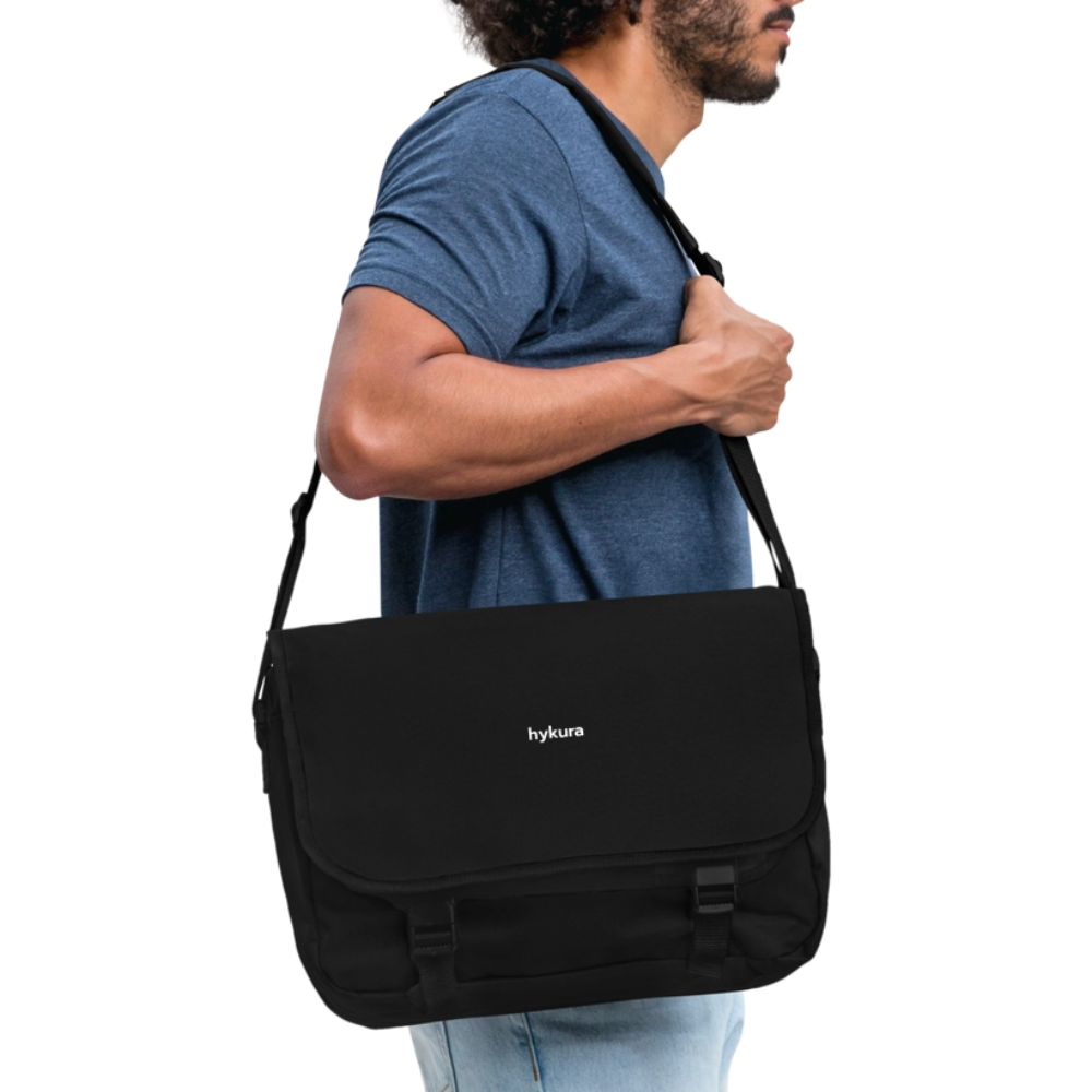 In black and worn by a man, the Hykura Stride Bag offers adjustable comfort, zip-secure storage, and tough polyester built for daily use.