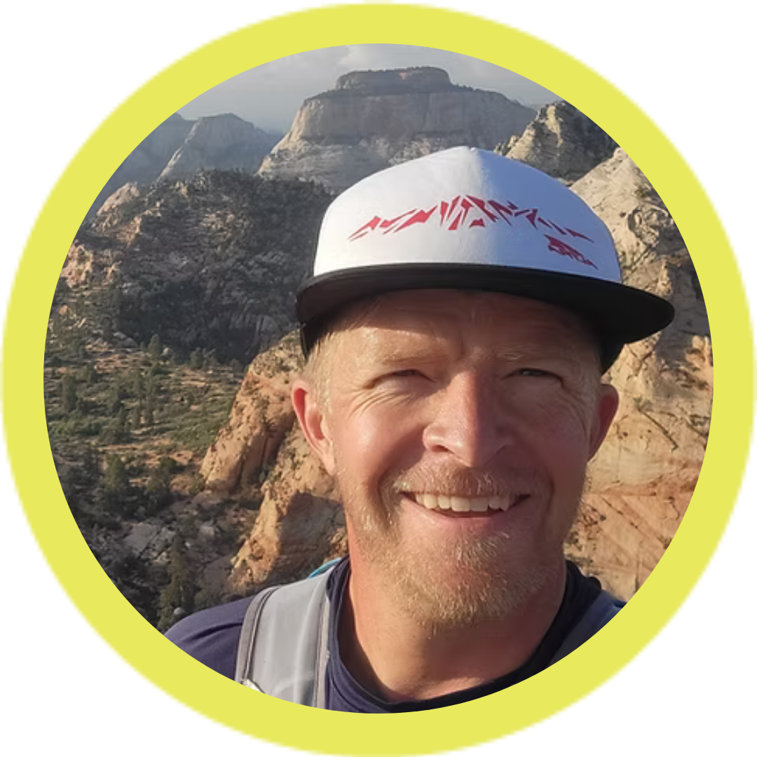 Man wearing a cap with mountains in the background.