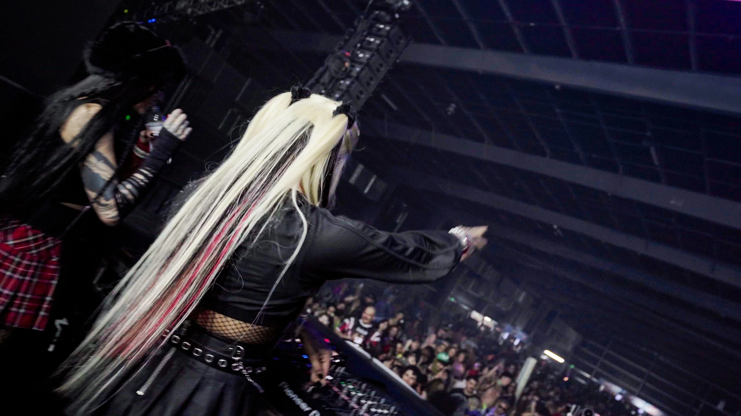 The image shows a concert scene with two female performers standing on stage. Hexxa b2b Sythyst