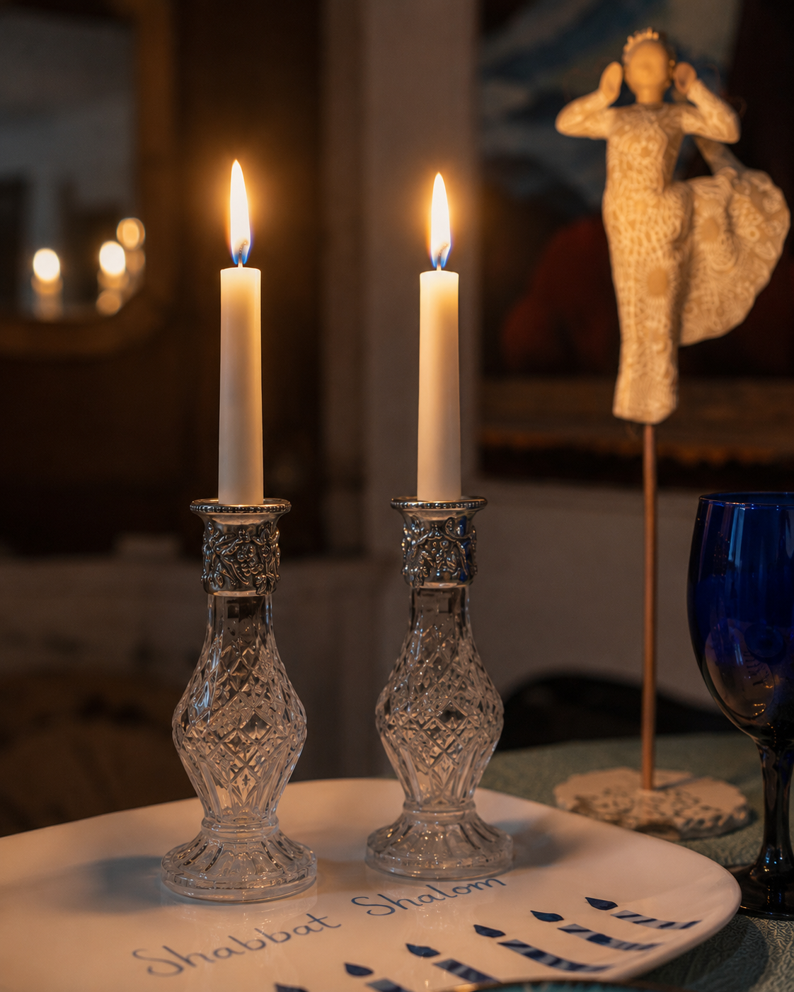 Close-up of two glowing Shabbat candles in ornate glass candlesticks, marking the beginning of Friday evening rest.