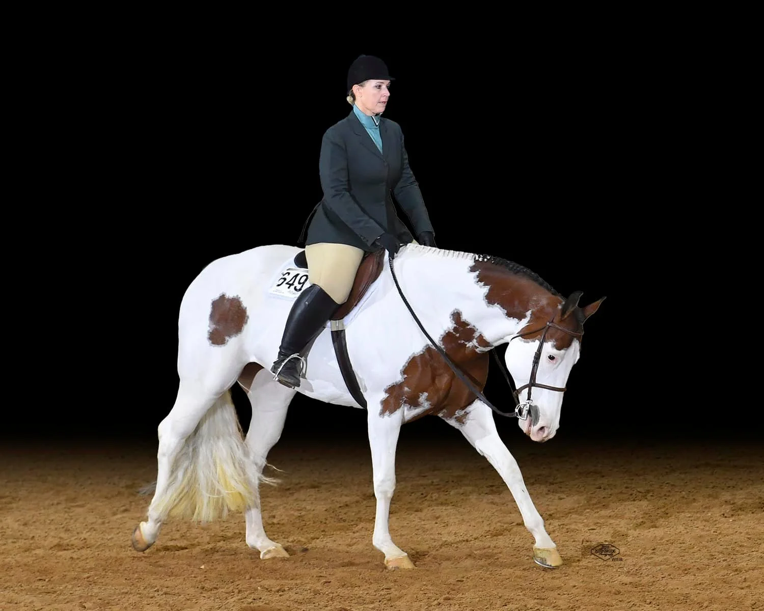 Rider on a white and brown paint horse performing in an equestrian event against a black background.