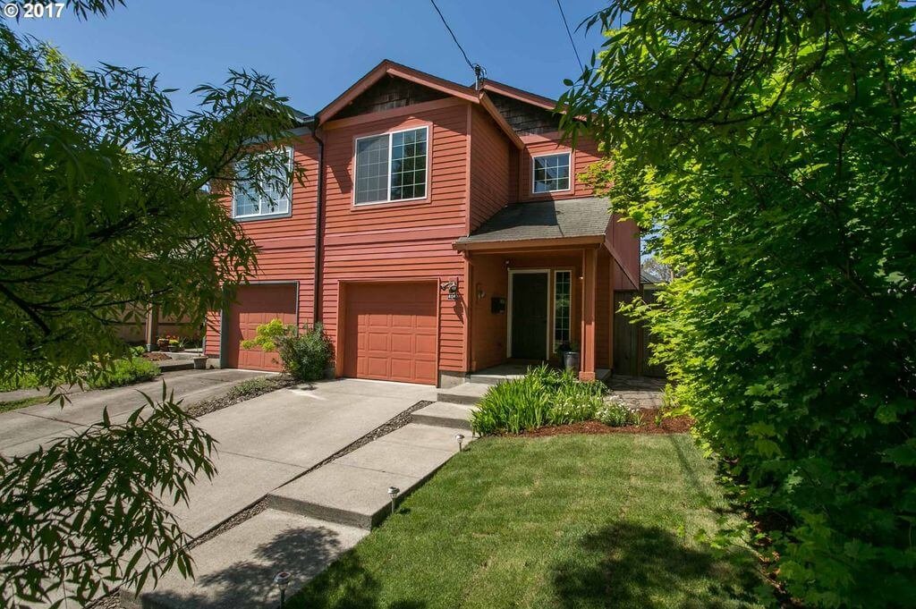 Two-story red townhouse in Portland, OR with garage and garden