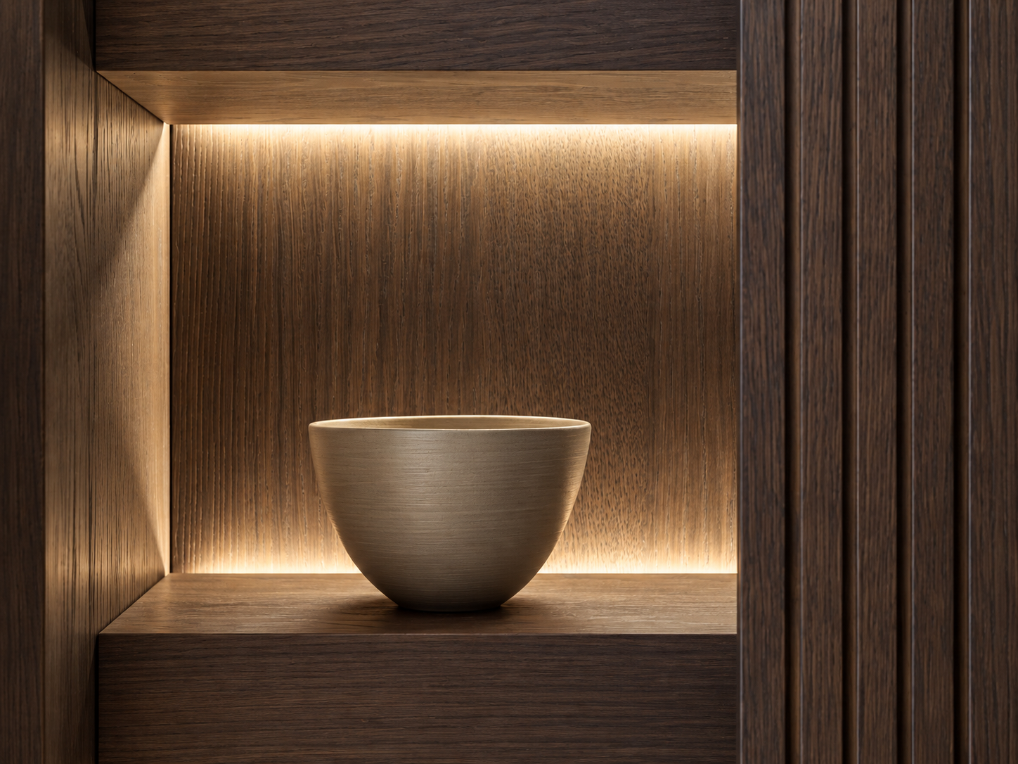 Minimalistische Holznische mit dekorativer Keramikschale, dunkler Holzstruktur und warmer indirekter LED-Beleuchtung als Detail eines hochwertigen Material- und Lichtkonzepts.