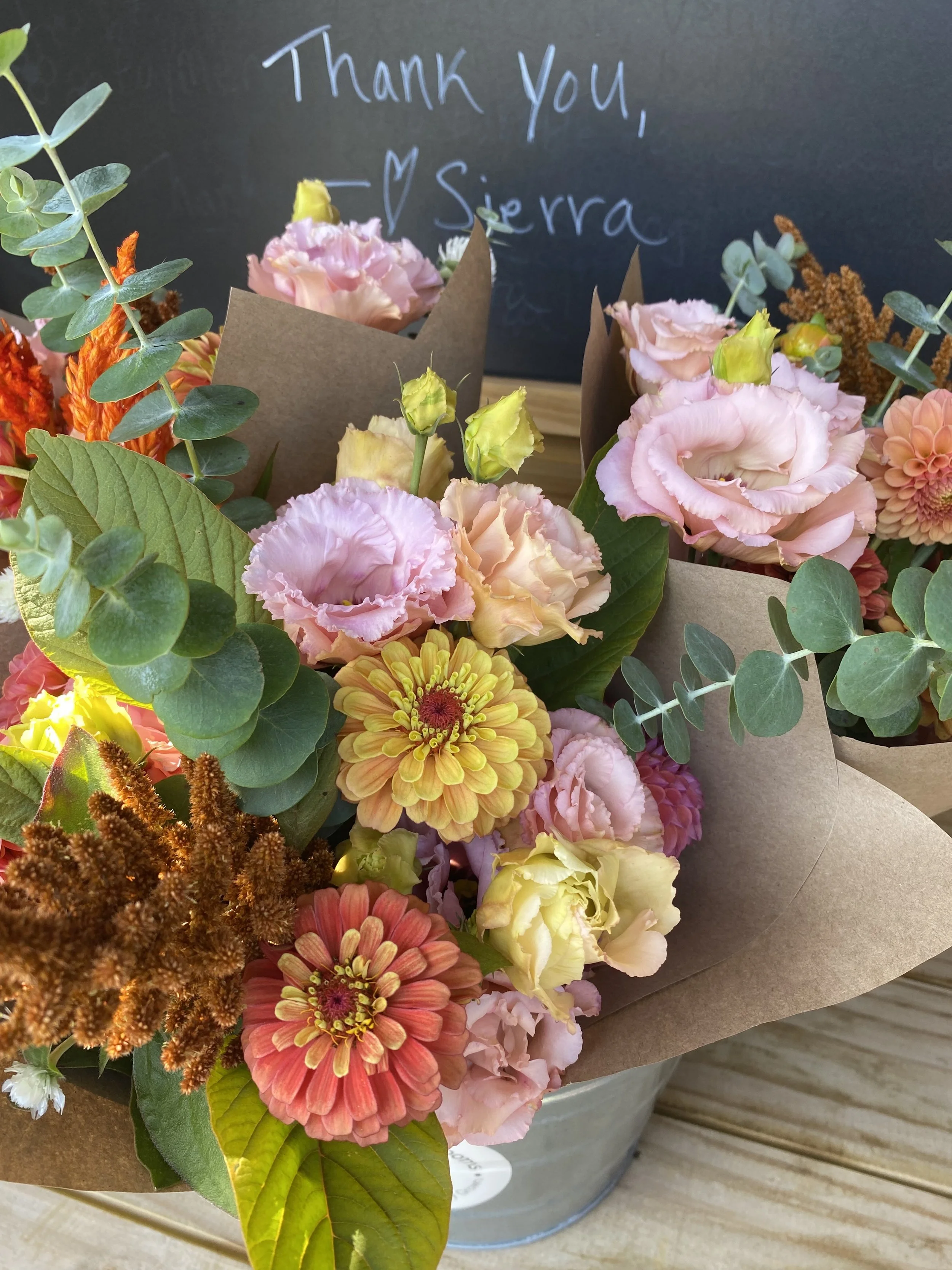 Bouquets of colorful flowers including zinnias and eucalyptus in brown paper wrapping.