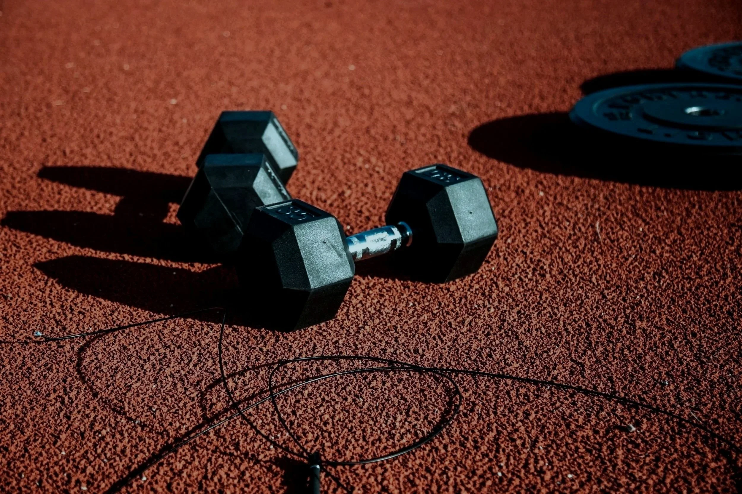 Dumbbell and weight plates on a red running track.