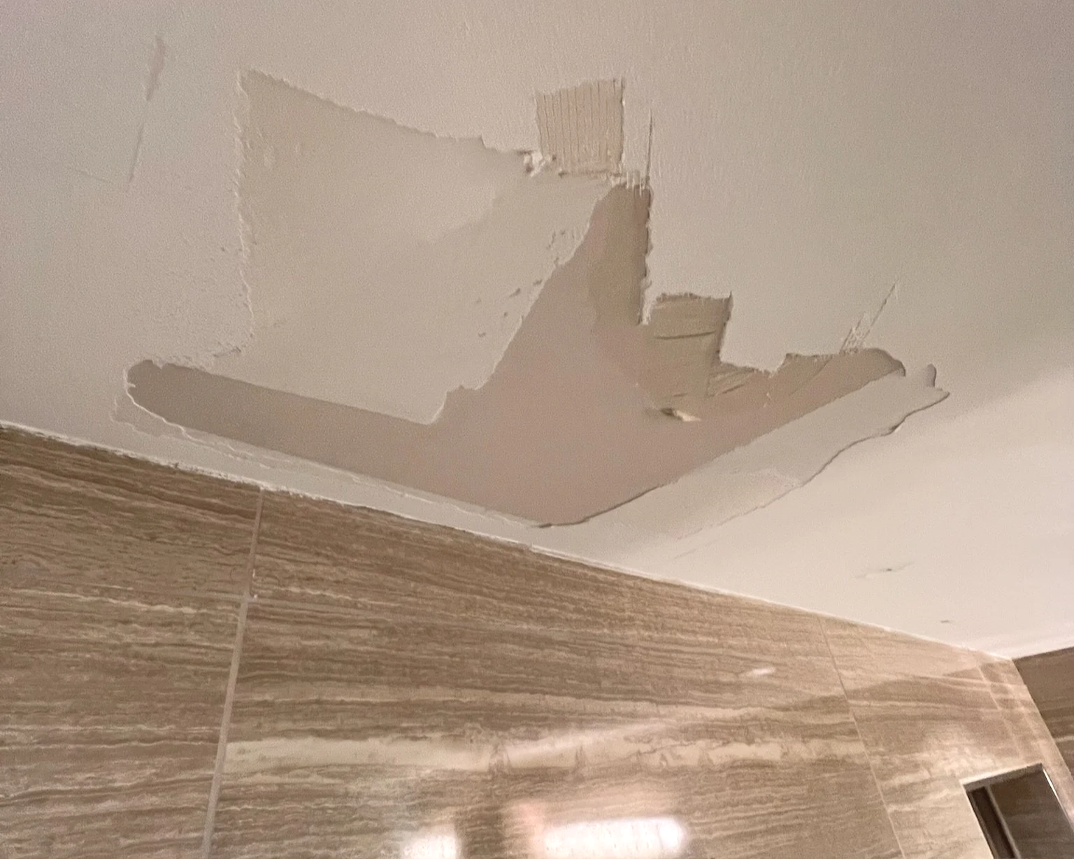 Peeling back bathroom ceiling drywall to reveal much-needed repairs from poor prior work