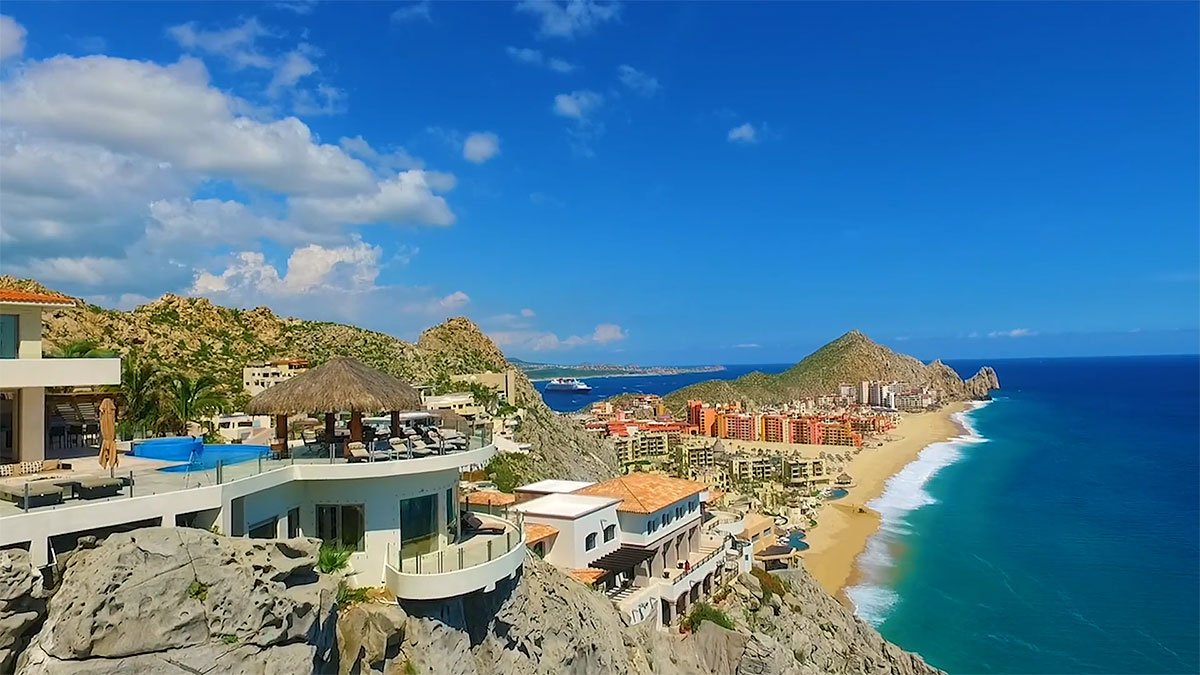 Coastal view of luxury villas and resorts along a sandy beach with a clear blue sky and ocean in the background.