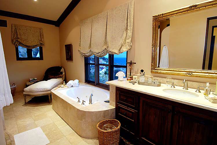 Luxury bathroom with a large bathtub, elegant vanity, gold-framed mirror, and scenic windows.