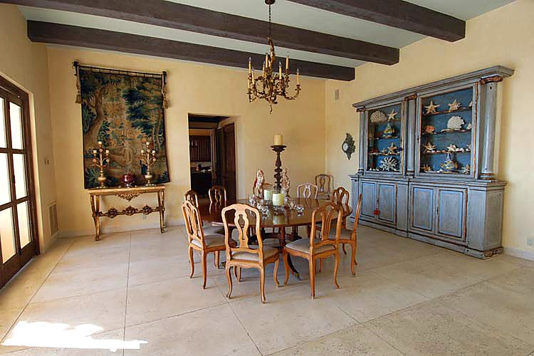 Elegant dining room with wooden table and chairs, ornate chandelier, decorative tapestry, and large cabinet displaying seashells.