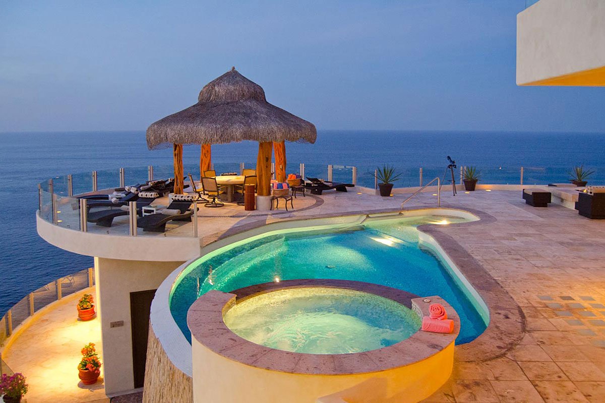 Rooftop terrace with a pool, hot tub, and thatched-roof seating area overlooking the ocean.